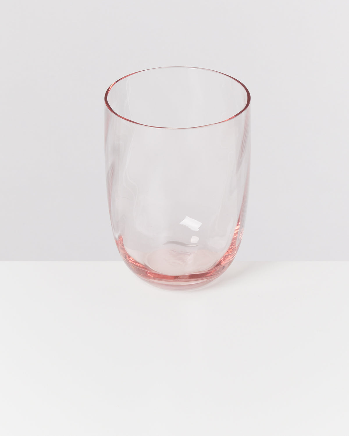 Durchsichtiges rosafarbenes Trinkglas auf einem weißen Tisch vor einem neutralen Hintergrund.