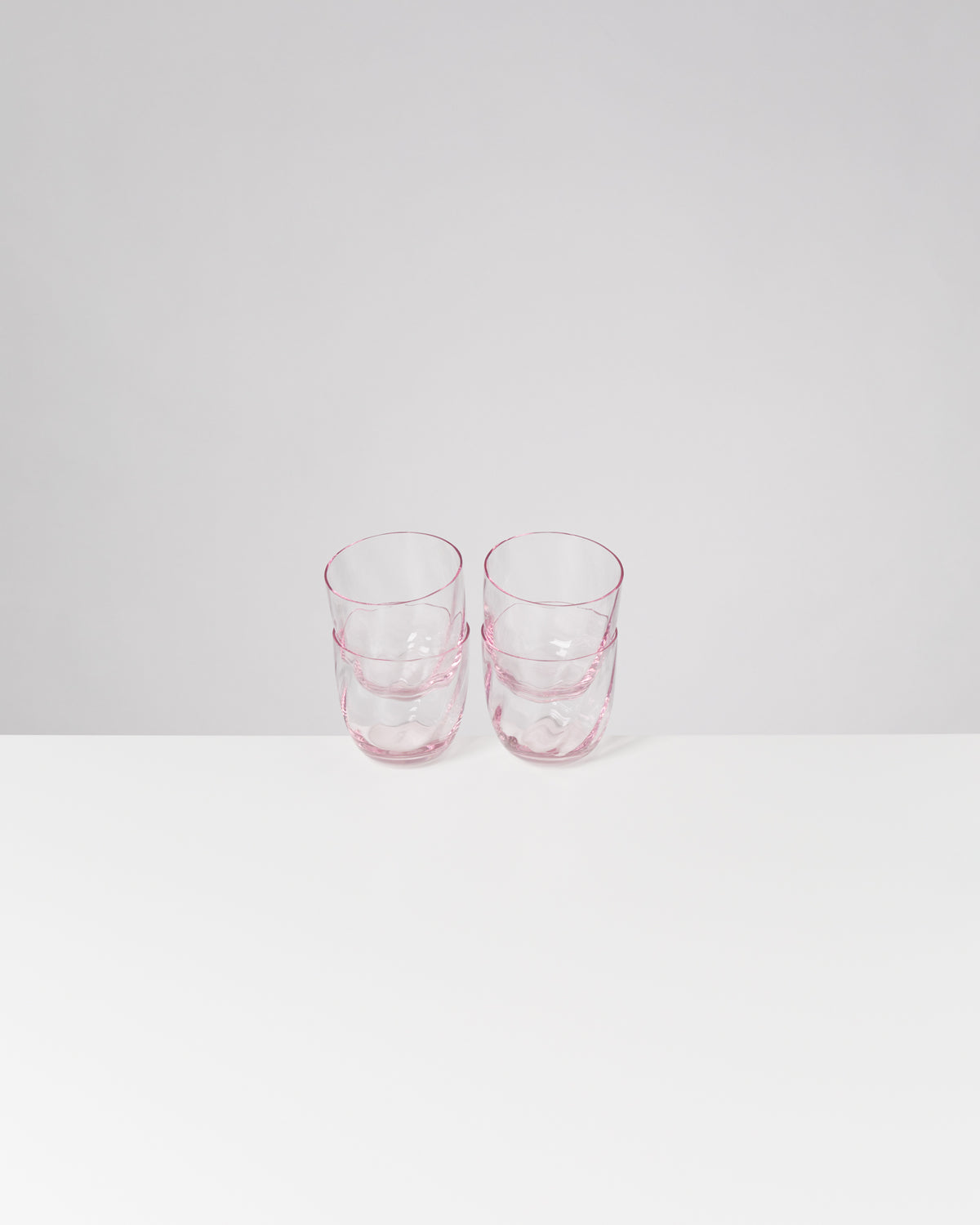 Zwei gestapelte, transparente rosa Gläser auf weißem Tisch vor grauer Wand.