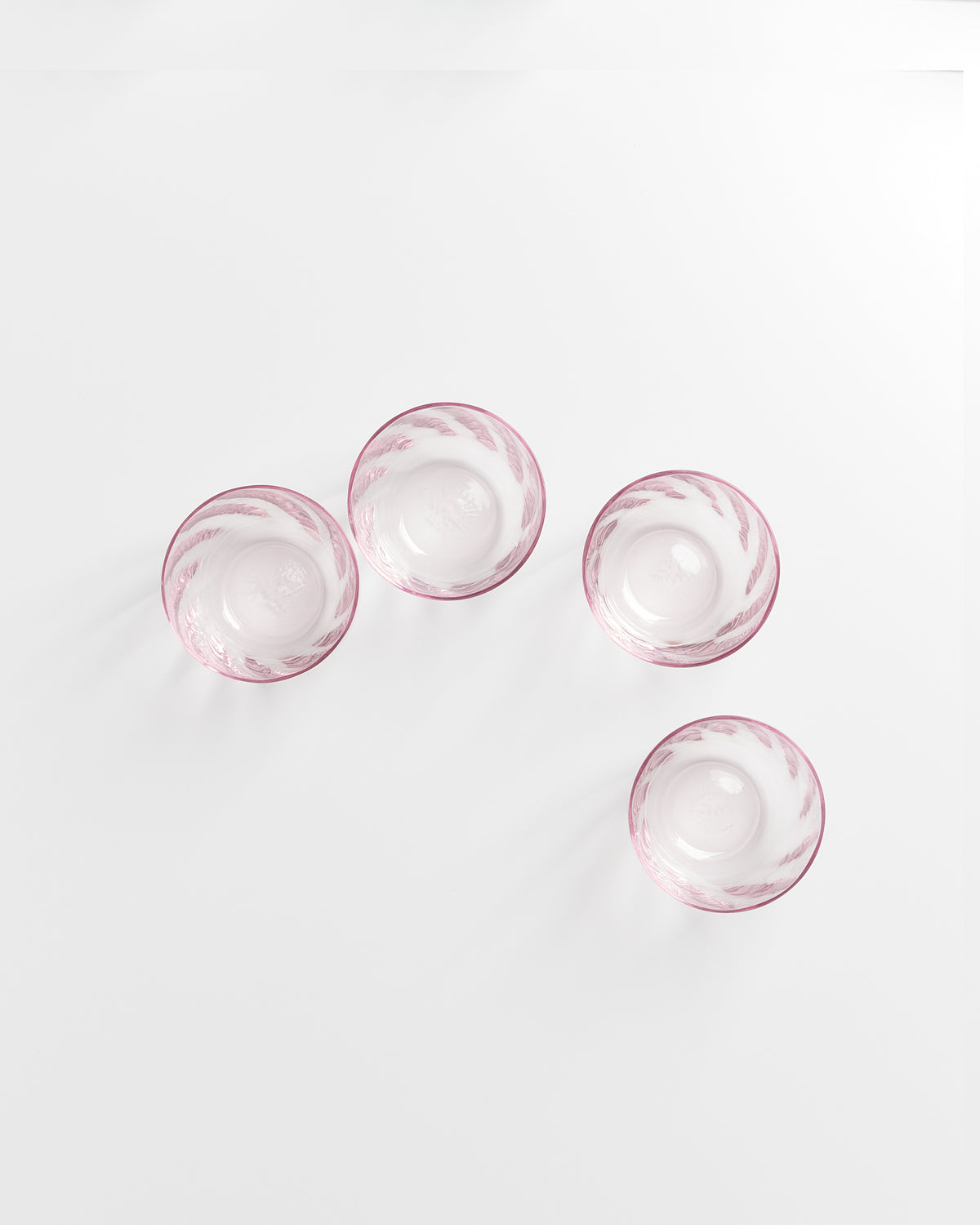 Vier rosafarbene Glasschalen mit weißem Muster stehen auf einem weißen Hintergrund.