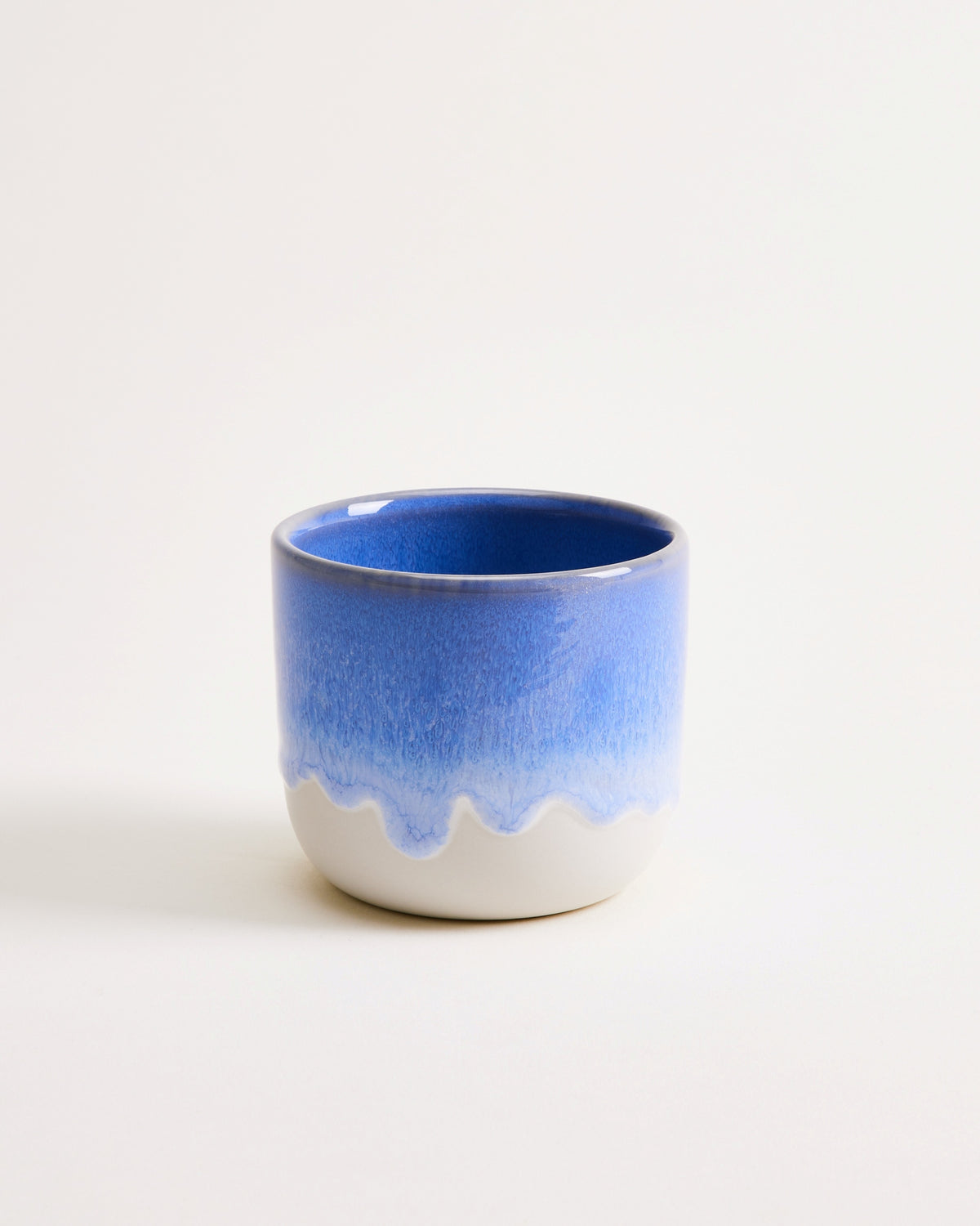 Blauer und weißer Keramikbecher mit gewelltem Design auf hellem Hintergrund.