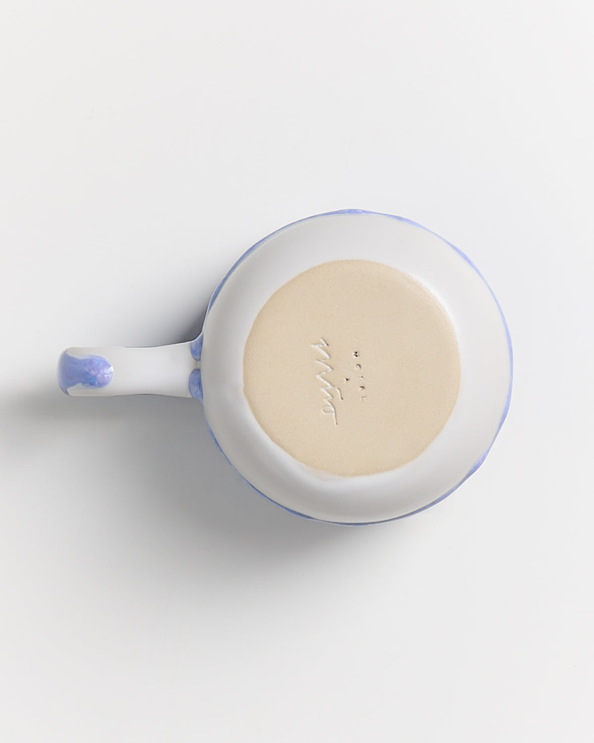 Weiße keramische Tasse mit blauem Griff, von oben fotografiert, zeigt die Unterseite mit eingraviertem Text.