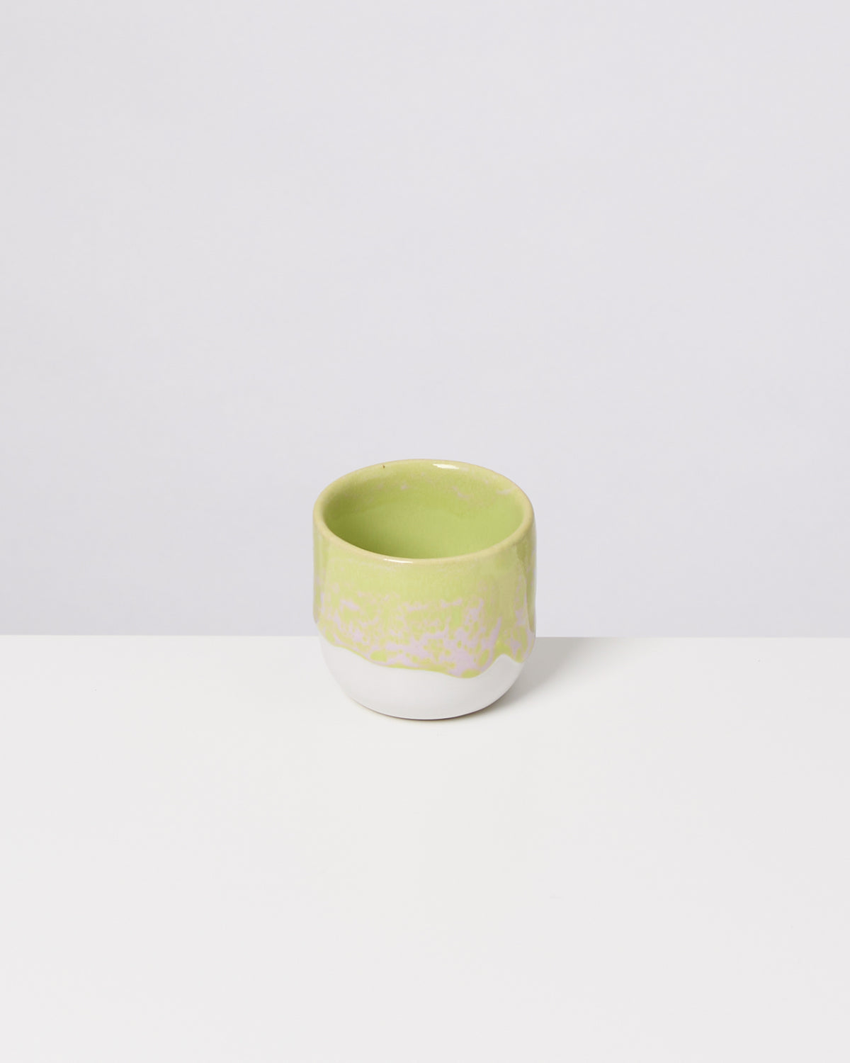 Grüne und weiße Keramiktasse mit unregelmäßigem Design, auf einem weißen Hintergrund.