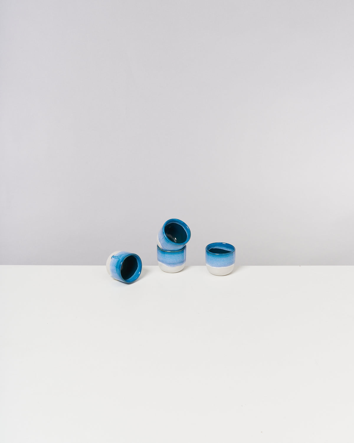 Vier blau-weiße Keramiktassen auf einem weißen Tisch vor einem grauen Hintergrund.