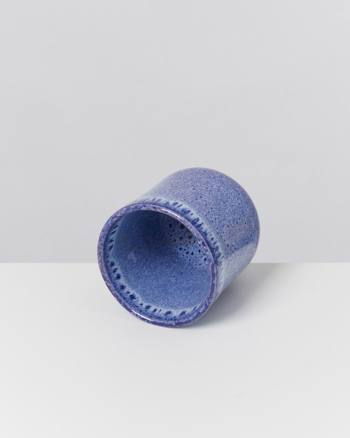 Blauer, keramischer Becher liegt auf der Seite auf einer weißen Oberfläche.