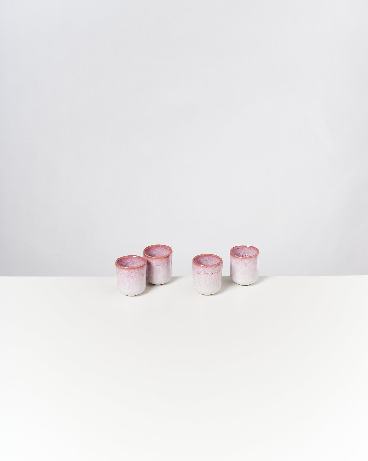 Vier kleine rosa-weiße Töpfe stehen auf einem weißen Tisch vor einem grauen Hintergrund.