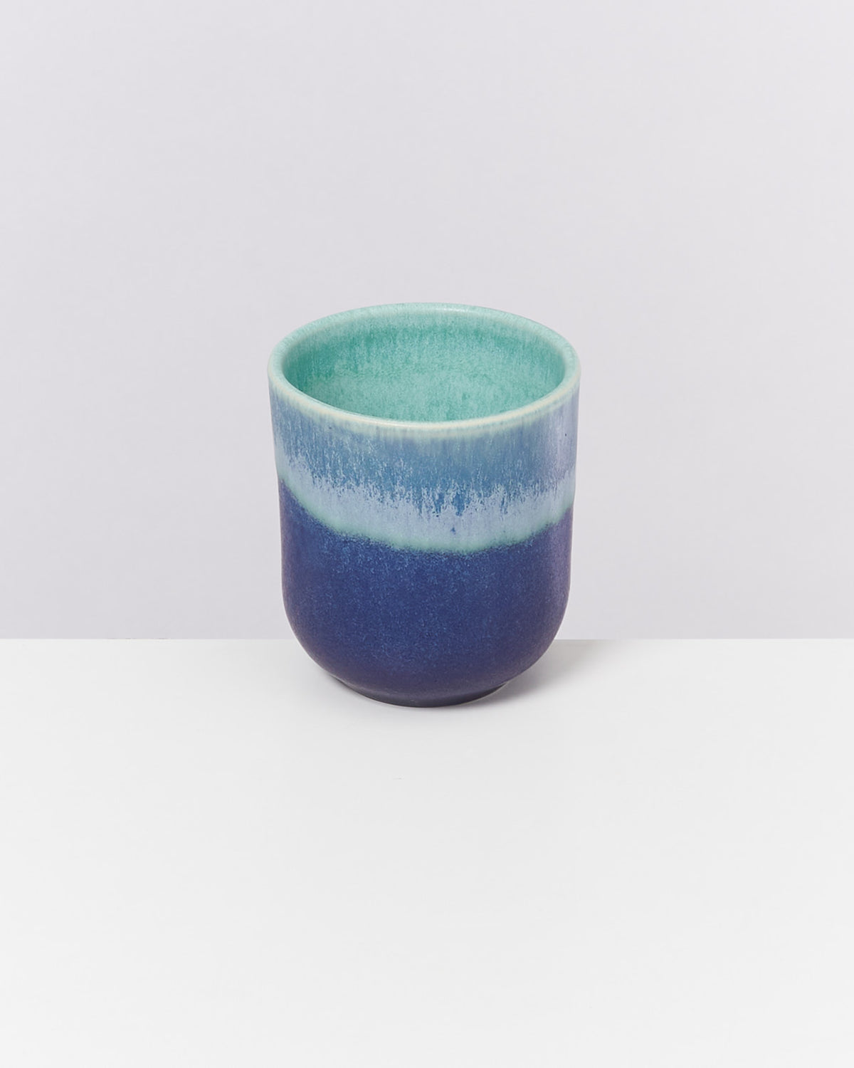 Blauer und türkiser Keramikbecher mit Farbverlauf auf weißem Hintergrund.