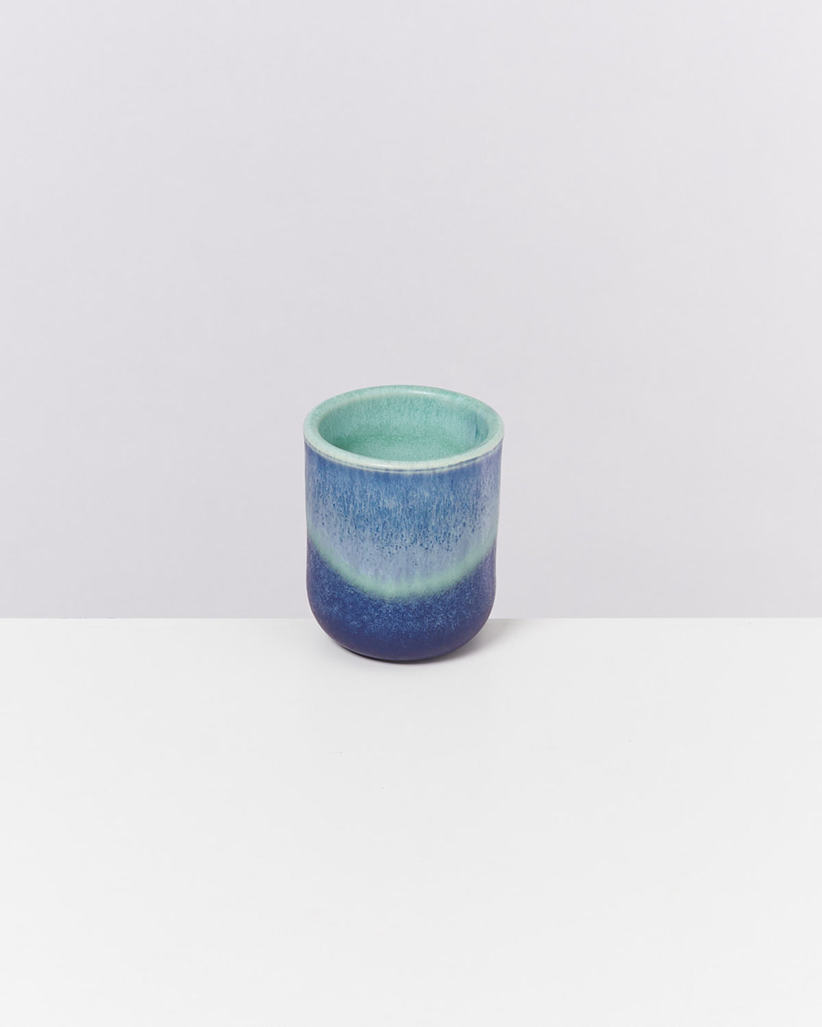Kleine blau-grüne Keramiktasse auf weißem Hintergrund.