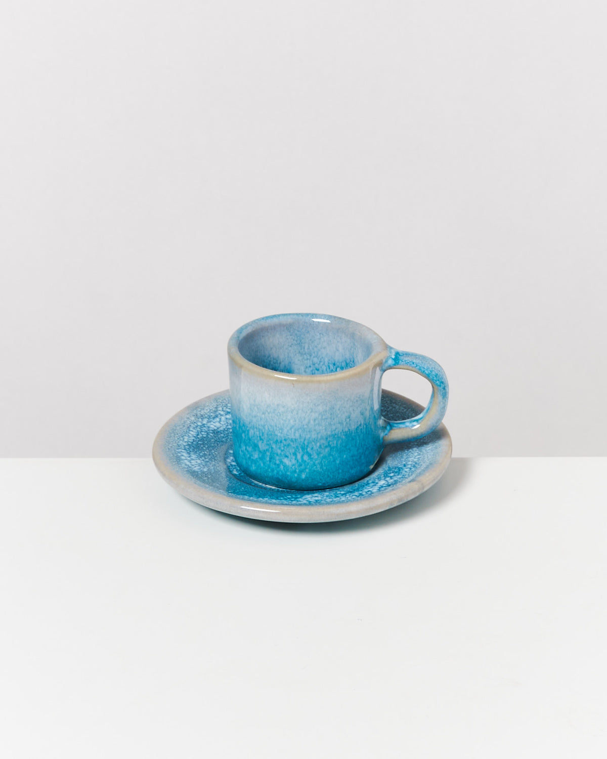 Blaue Keramiktasse auf passender Untertasse, auf weißem Untergrund.
