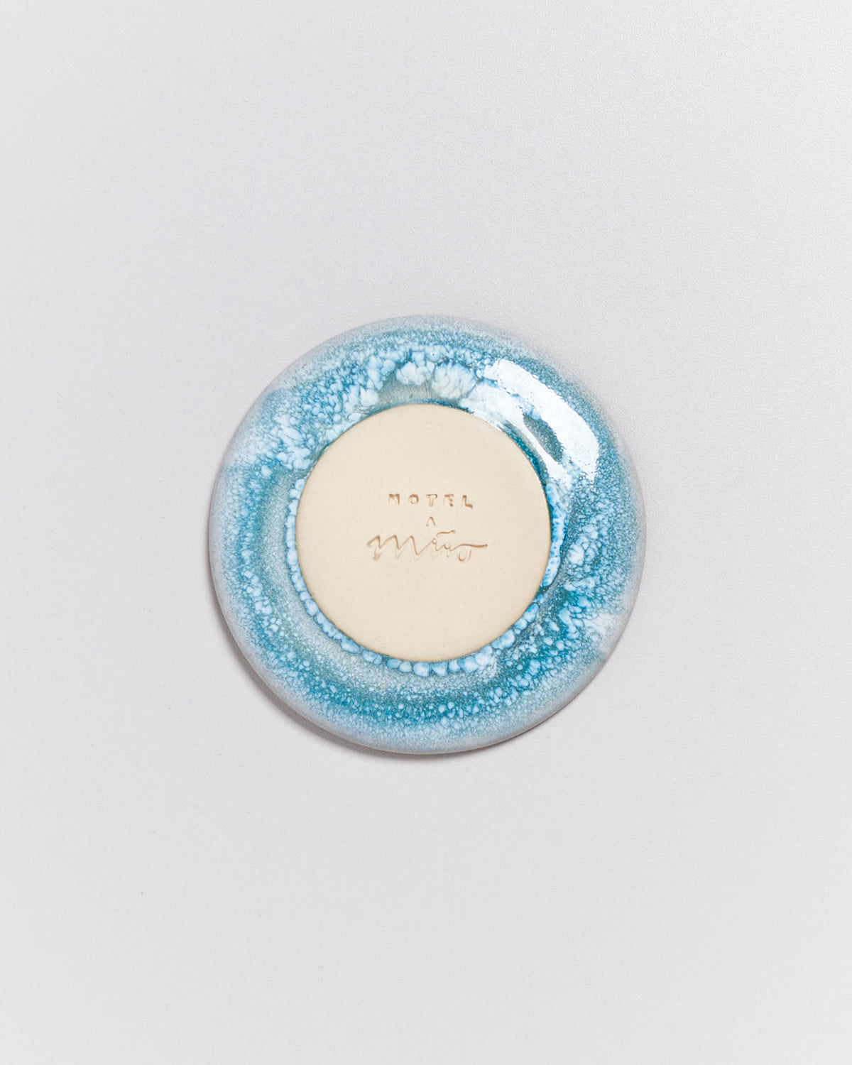 Runder Keramikgegenstand mit blau-weißer Glasur, in der Mitte beige mit Gravur.
