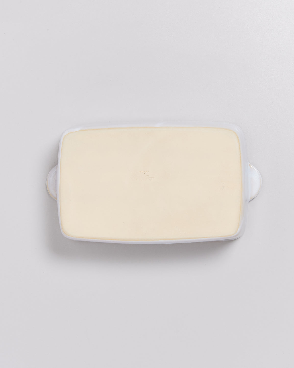 Rechteckige, weiße Butterdose mit hellem Inhalt, von oben auf einer hellgrauen Oberfläche fotografiert.