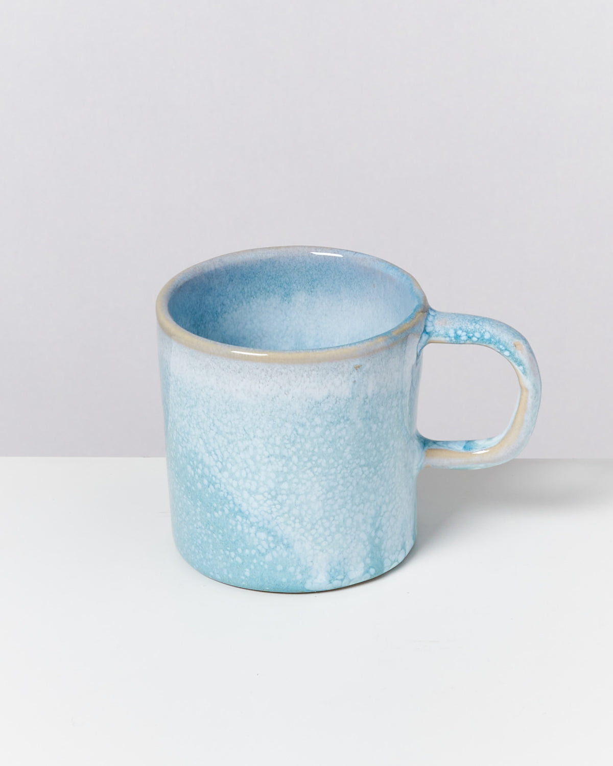 Himmelblaue Keramiktasse mit weißem Sprenkelmuster auf weißem Hintergrund.
