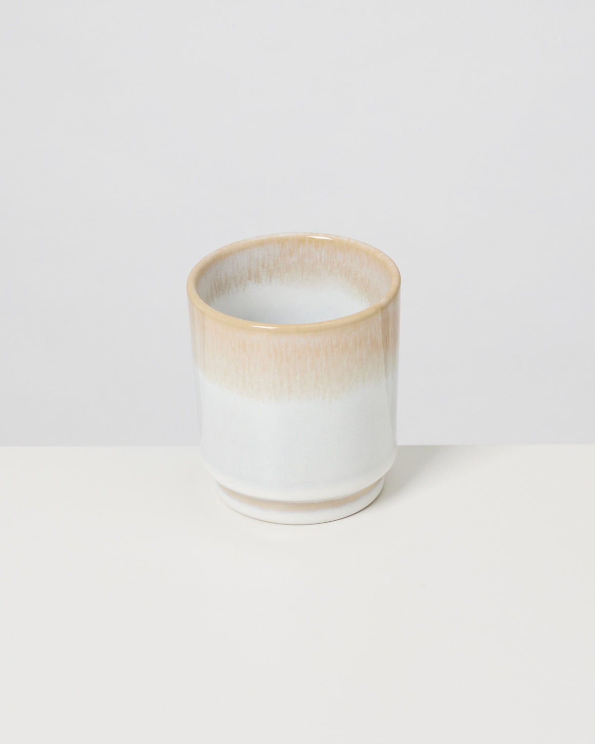 Keramikbecher mit beige-weißer Glasur auf weißem Hintergrund.
