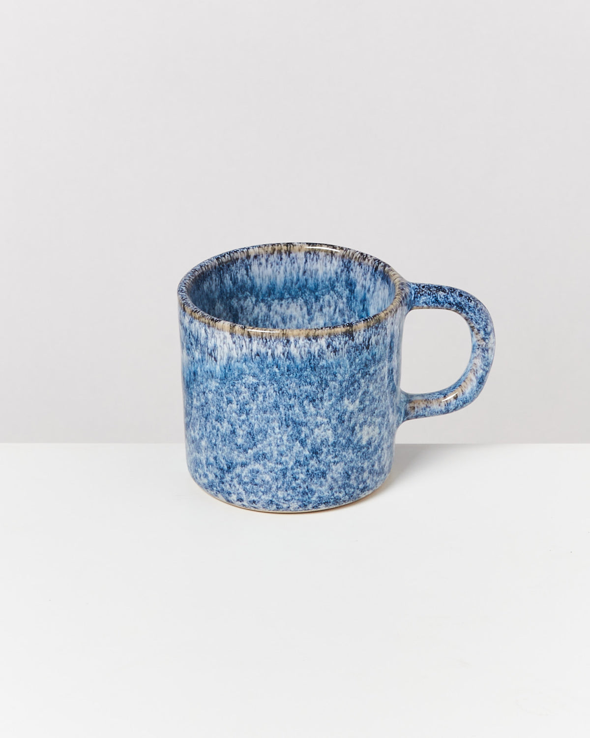 Blaue Keramiktasse mit gesprenkeltem Design steht auf einem weißen Hintergrund.
