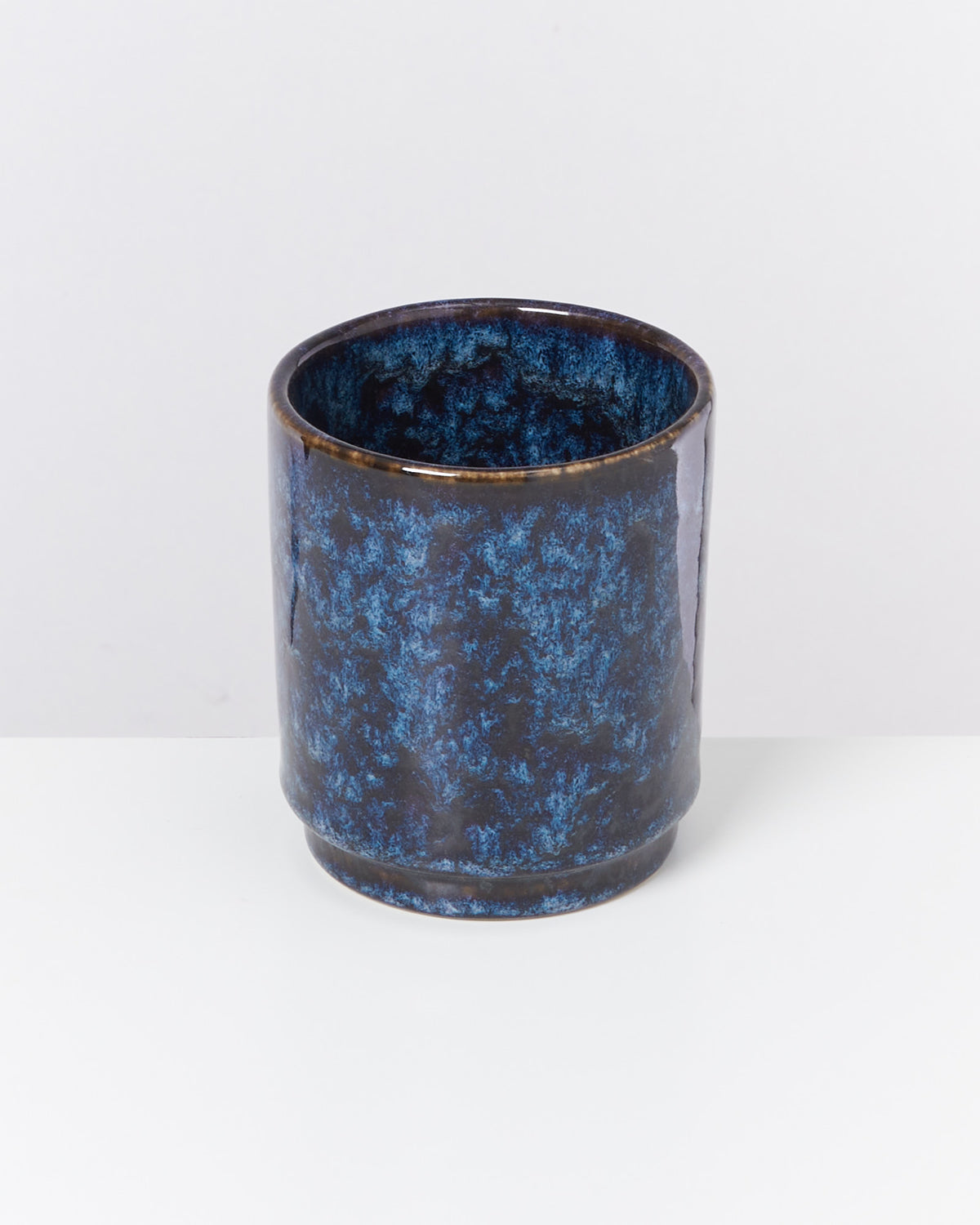 Blauer, zylindrischer Keramikbecher mit marmoriertem Muster auf weißem Hintergrund.