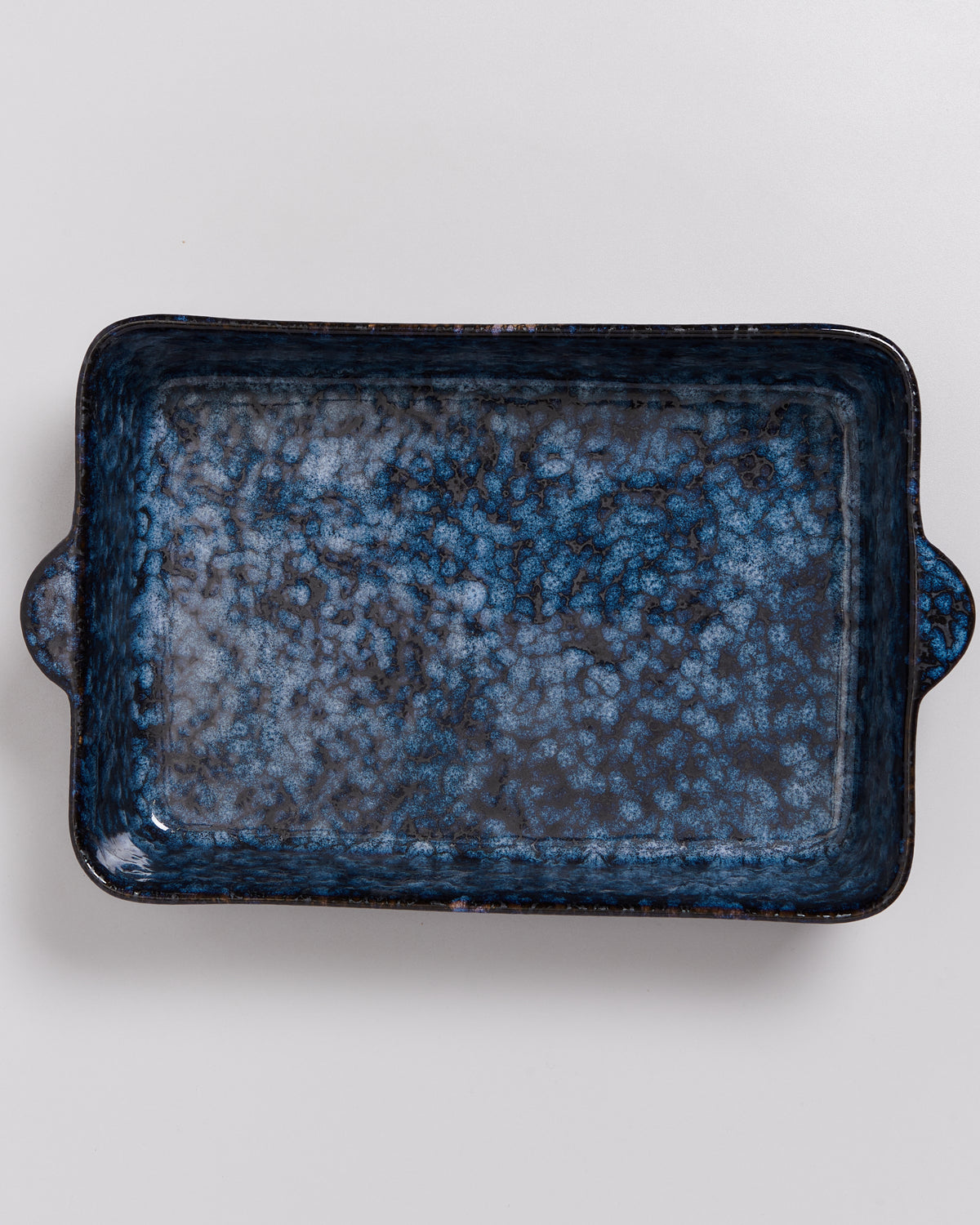 Rechteckige, blaue Keramikform mit speckigem Muster und kleinen Griffen auf einem hellen Hintergrund.