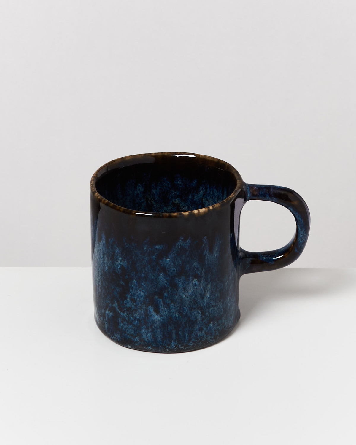 Dunkelblaue Keramiktasse mit schwarzem Rand und Henkel, auf einem weißen Hintergrund.