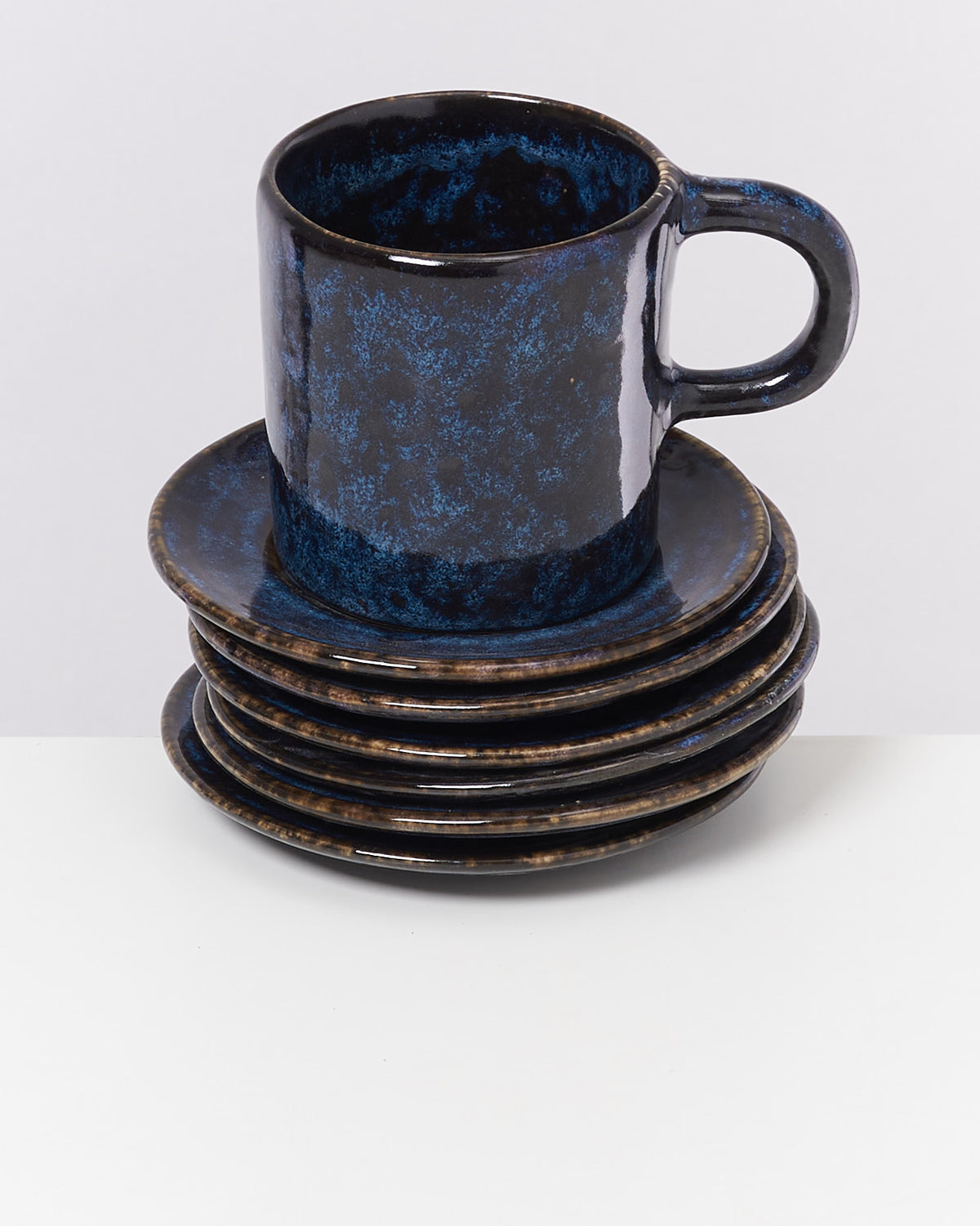 Dunkelblaue Keramiktasse steht auf einem Stapel dunkler Teller auf einem weißen Hintergrund.