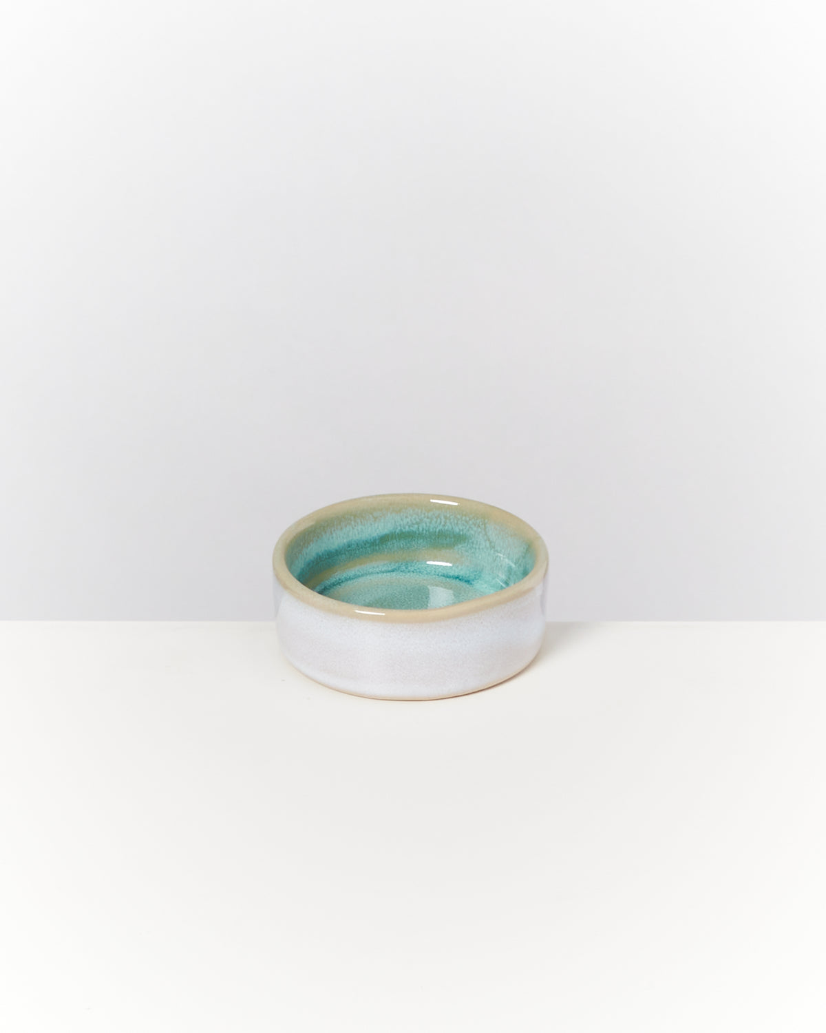 Keramikschale mit blau-grüner Innenlasur auf einem weißen Hintergrund.