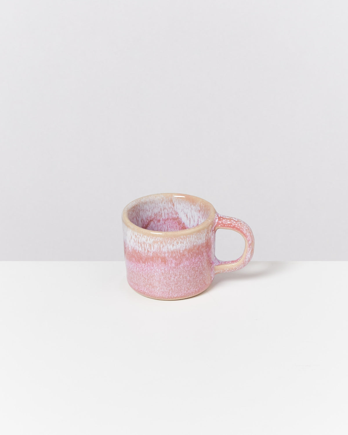 Rosa-weiße Keramiktasse auf weißem Hintergrund mit einem einfachen Henkel.