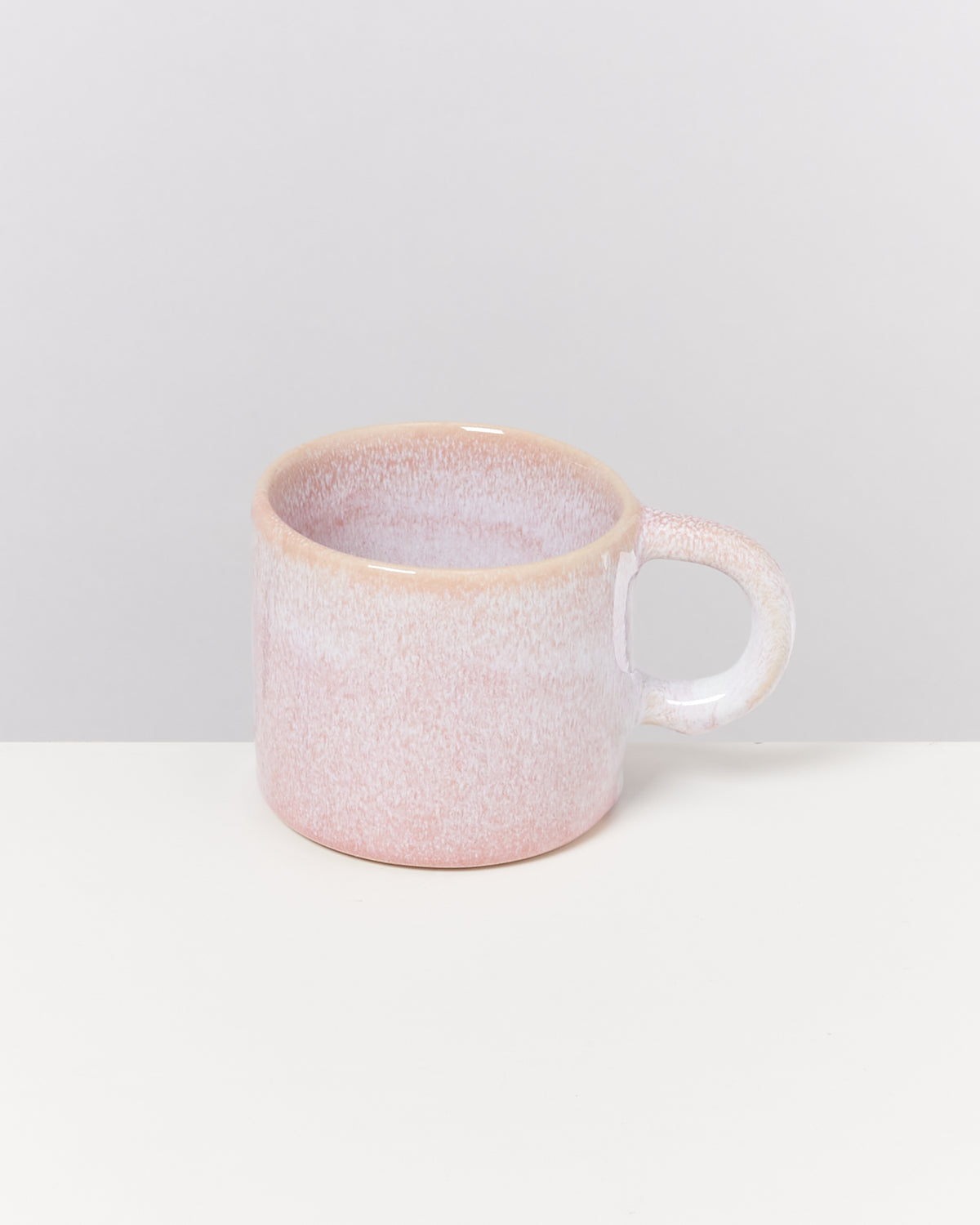 Eine pastellrosa Tasse mit Henkel steht auf einem weißen Hintergrund.