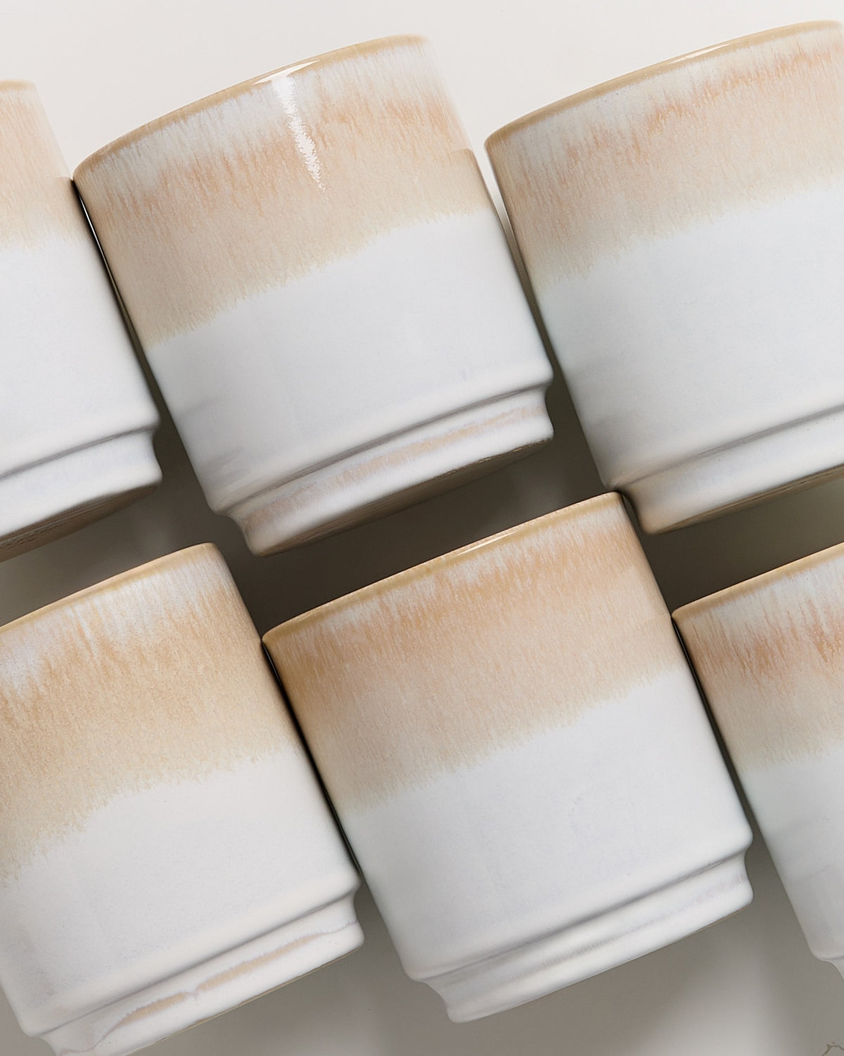 Sechs weiß-beige Tassen mit glattem Verlaufsmuster in seitlicher Ansicht auf einem hellen Hintergrund.