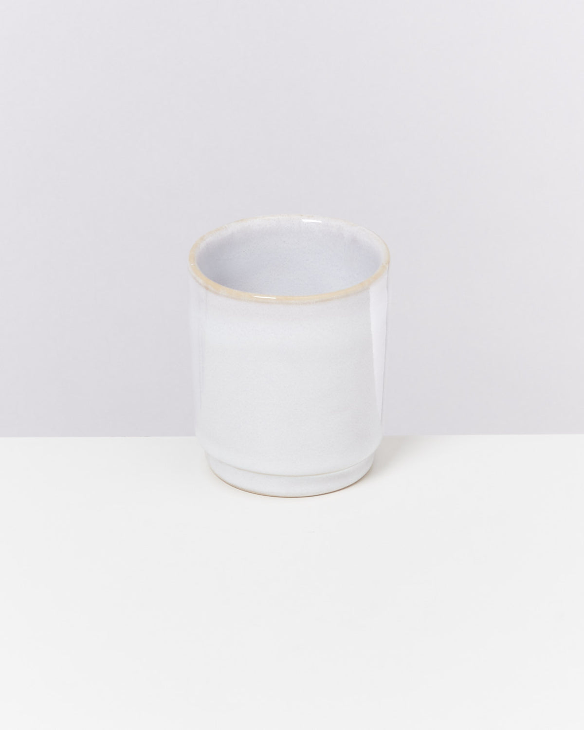 Weiße Keramiktasse auf einem weißen Tisch vor einem grauen Hintergrund.