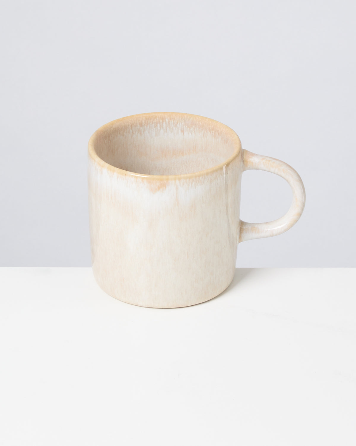Beiger Keramikbecher mit Henkel auf weißem Hintergrund.