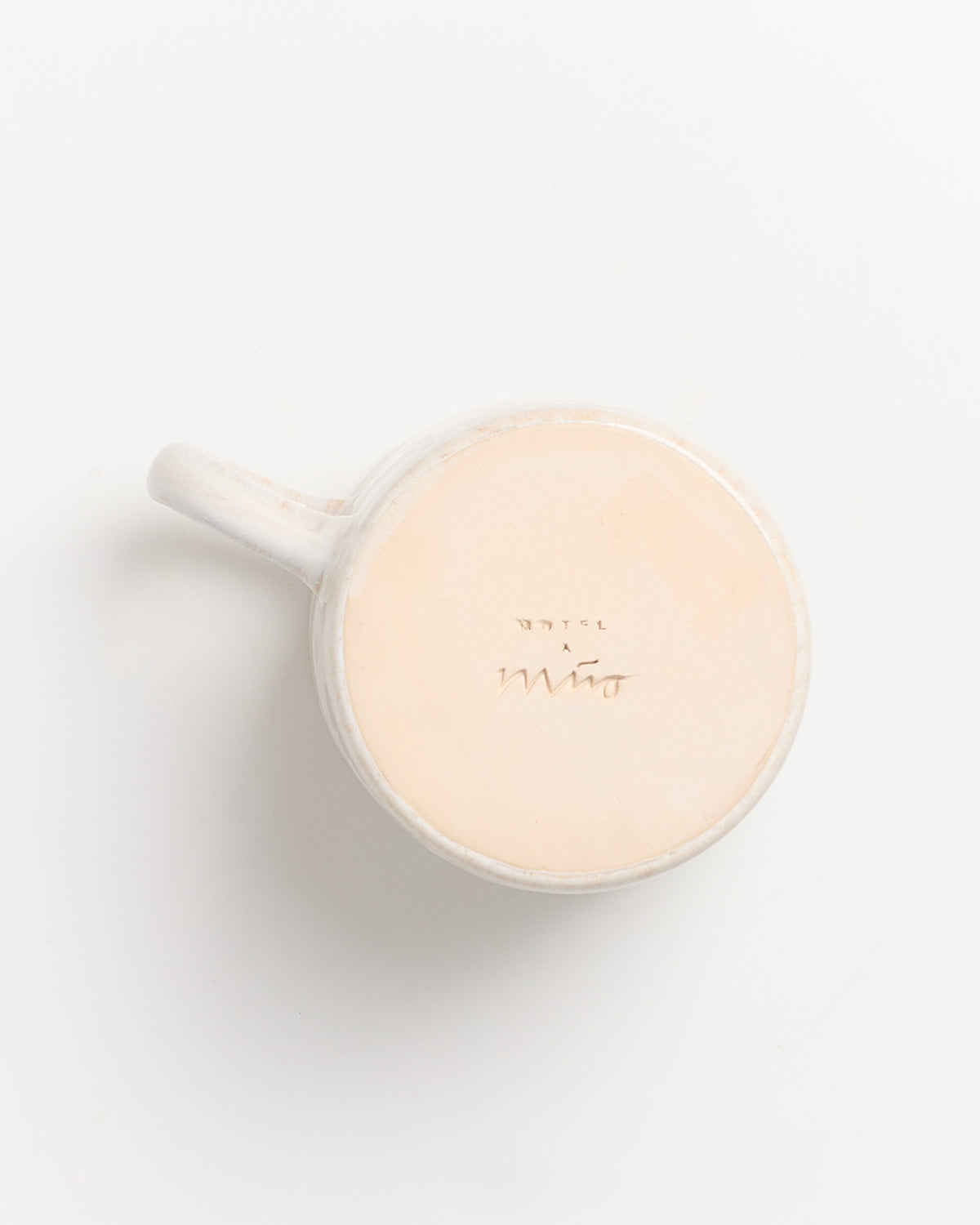 Weiße Tasse aus Keramik, von unten fotografiert, mit eingeprägter Schrift auf dem Boden.