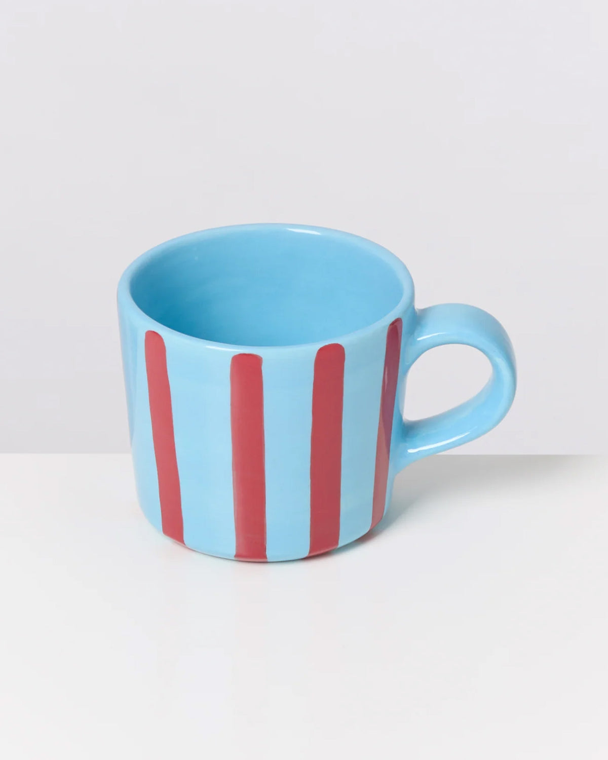 Hellblaue Tasse mit roten vertikalen Streifen auf einem weißen Hintergrund.