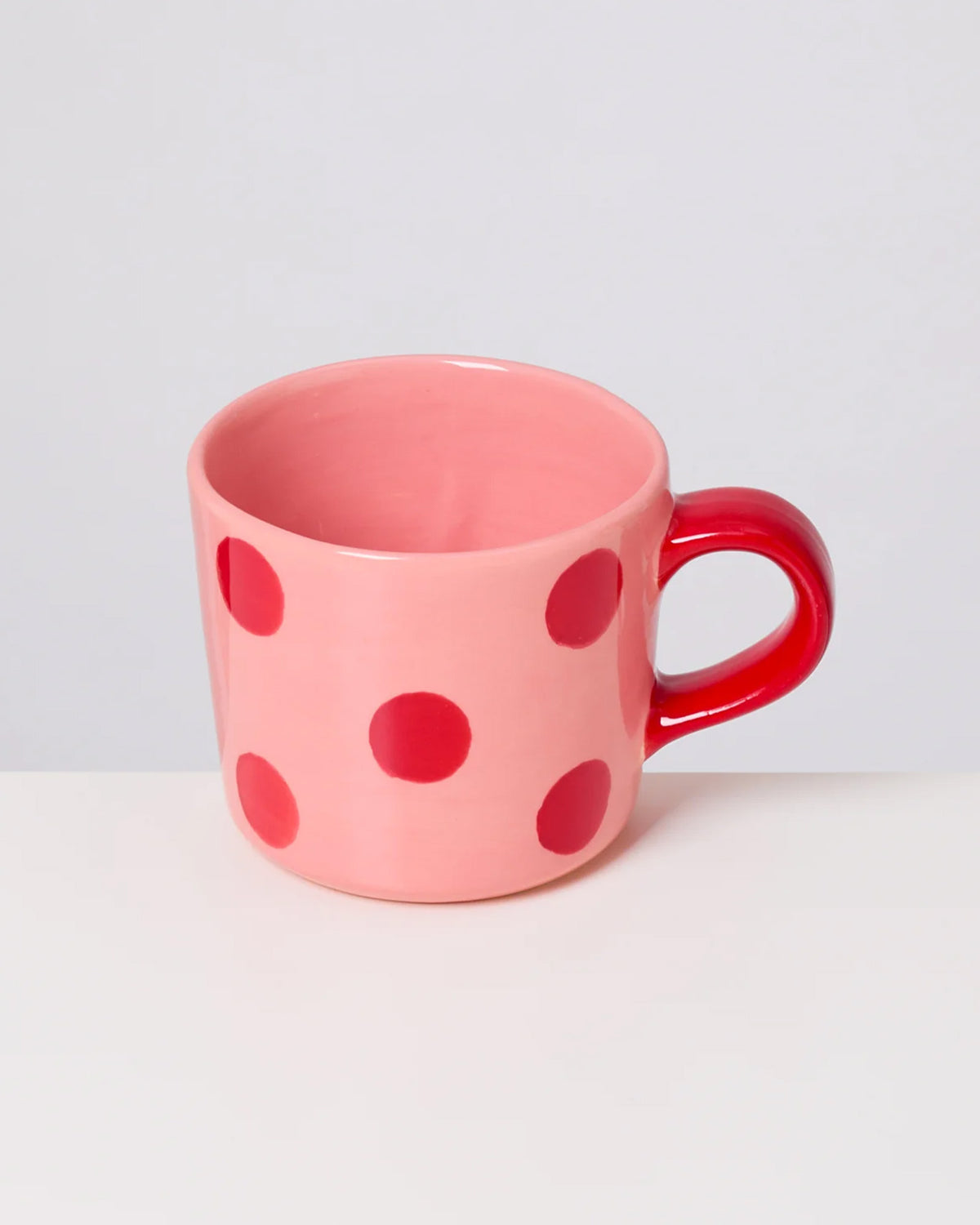 Rosa Tasse mit roten Punkten und einem roten Henkel auf weißem Hintergrund.