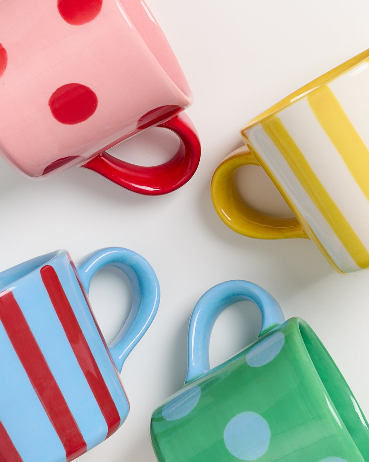 Vier bunte Tassen mit verschiedenen Mustern: Rot mit Punkten, Gelb gestreift, Blau gestreift und Grün mit Punkten.