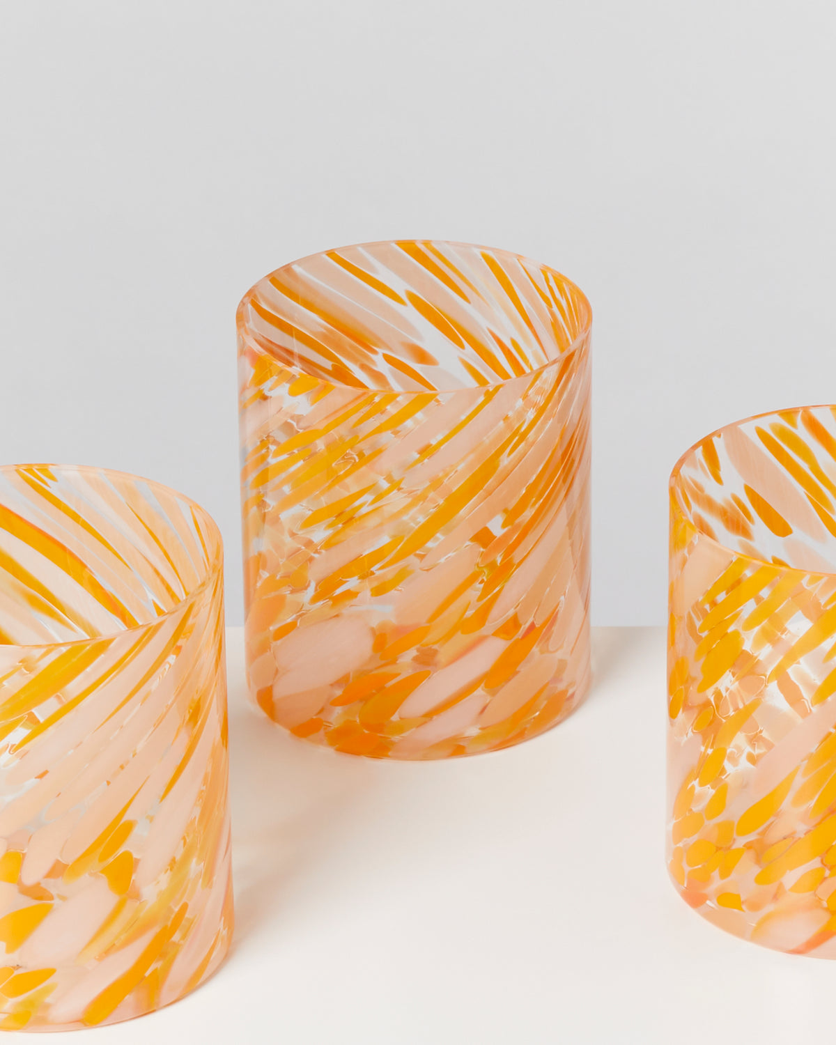 Drei zylindrische Vasen mit orange-weißen Wirbelmustern auf einem weißen Hintergrund.