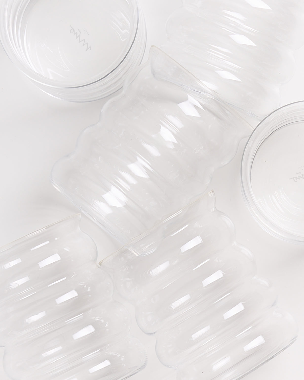 Mehrere durchsichtige Glasgefäße mit wellenförmigem Design auf einer weißen Oberfläche.