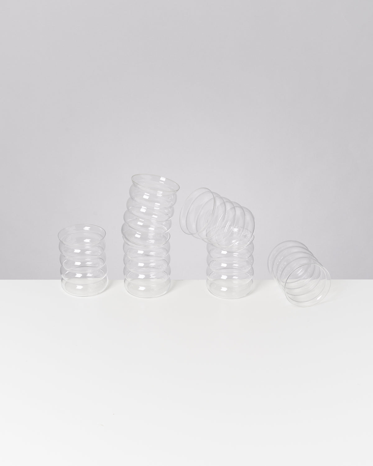 Drei ineinander gestapelte, durchsichtige Plastikbecher liegen auf einem weißen Tisch vor einem grauen Hintergrund.
