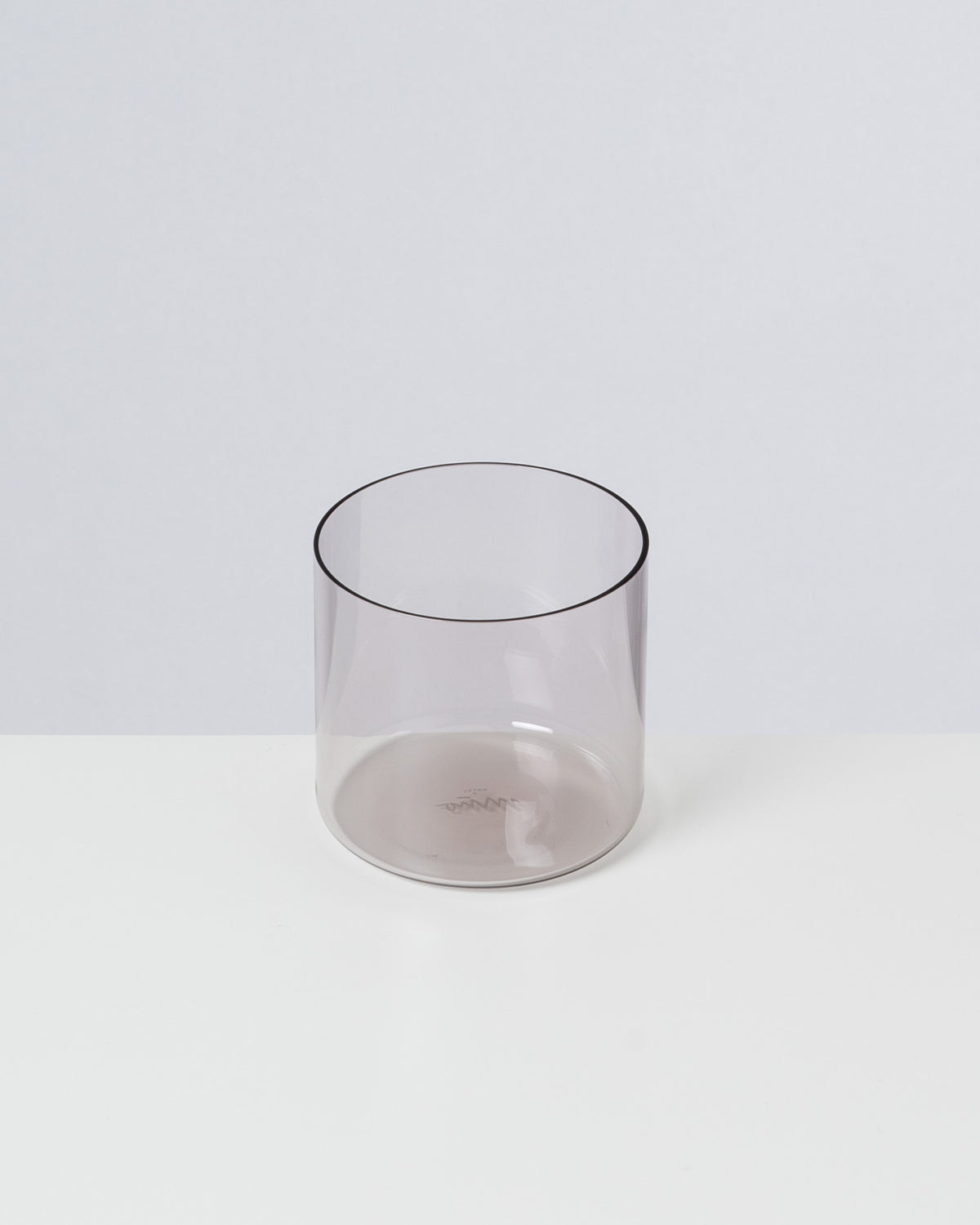 Ein durchsichtiges, graues Glas steht auf einer weißen Oberfläche vor einem grauen Hintergrund.