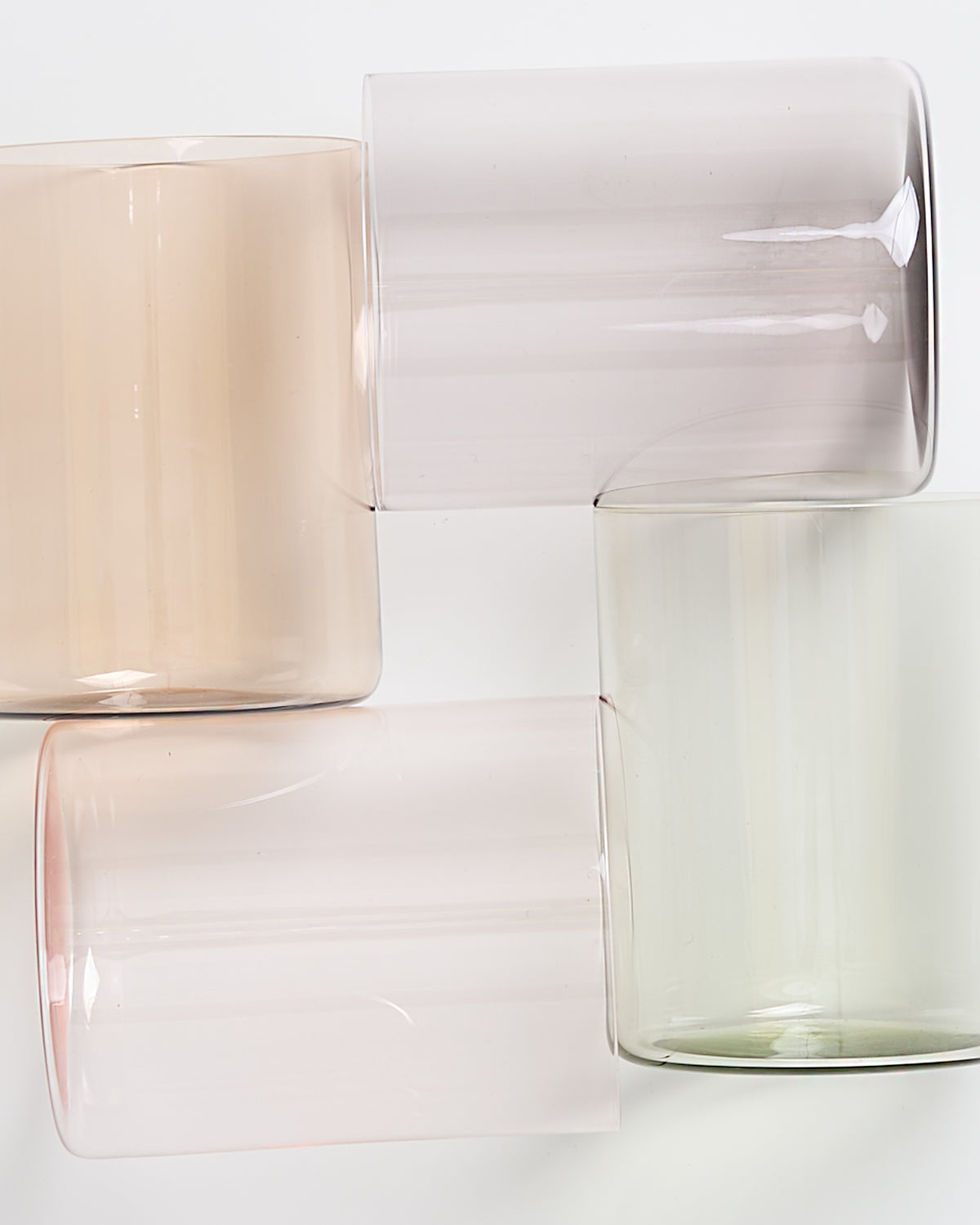 Vier farbige, transparente Gläser liegen seitlich und ineinander verschachtelt auf einer weißen Oberfläche.