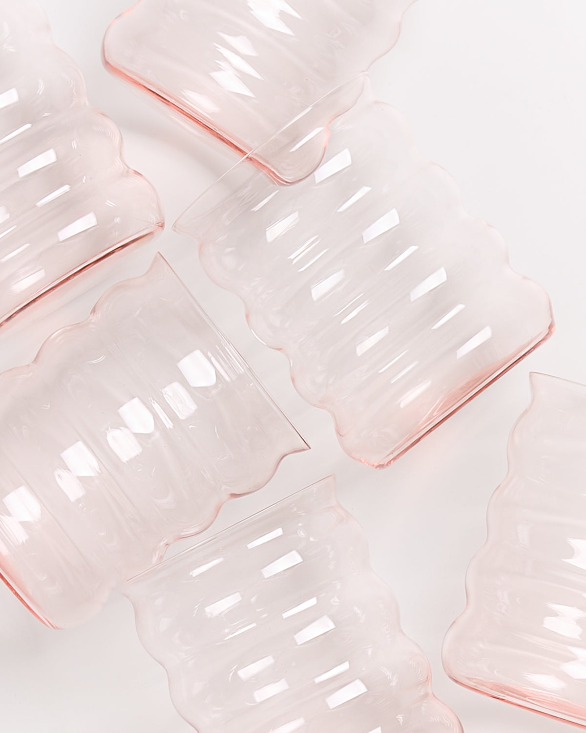 Wellenförmige, transparente rosa Gläser liegen diagonal auf einer weißen Oberfläche.