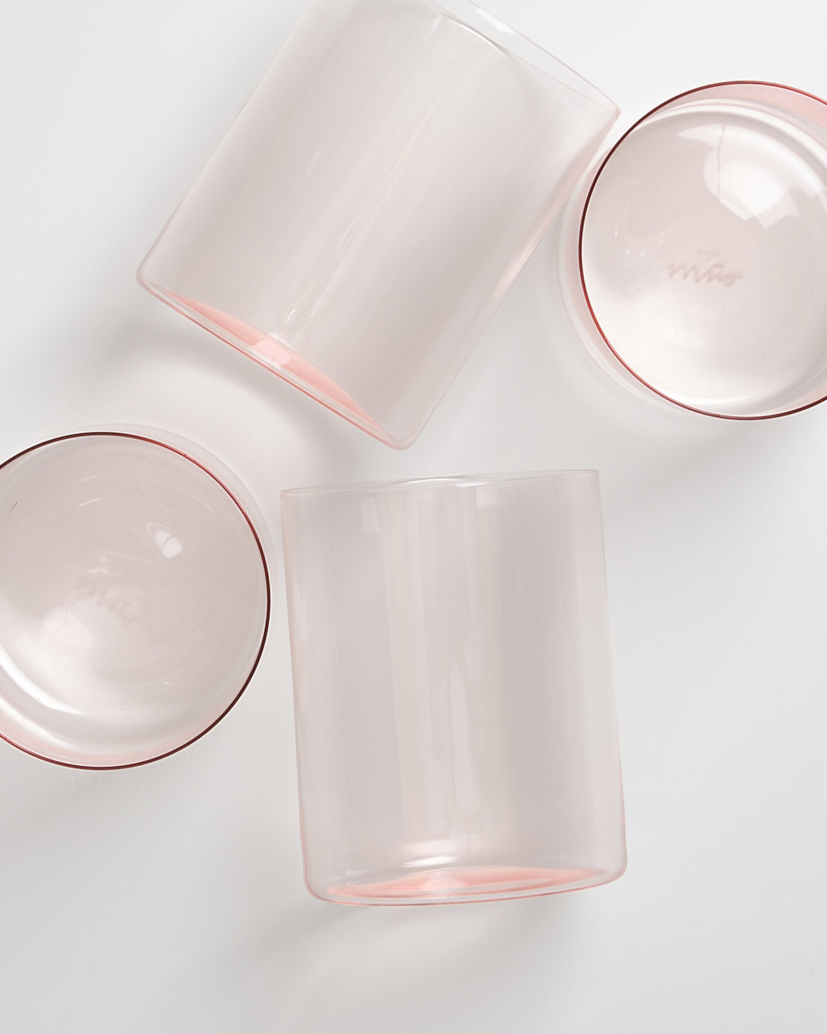 Vier teilweise transparente Gläser mit einem rosa Schimmer auf weißem Hintergrund.