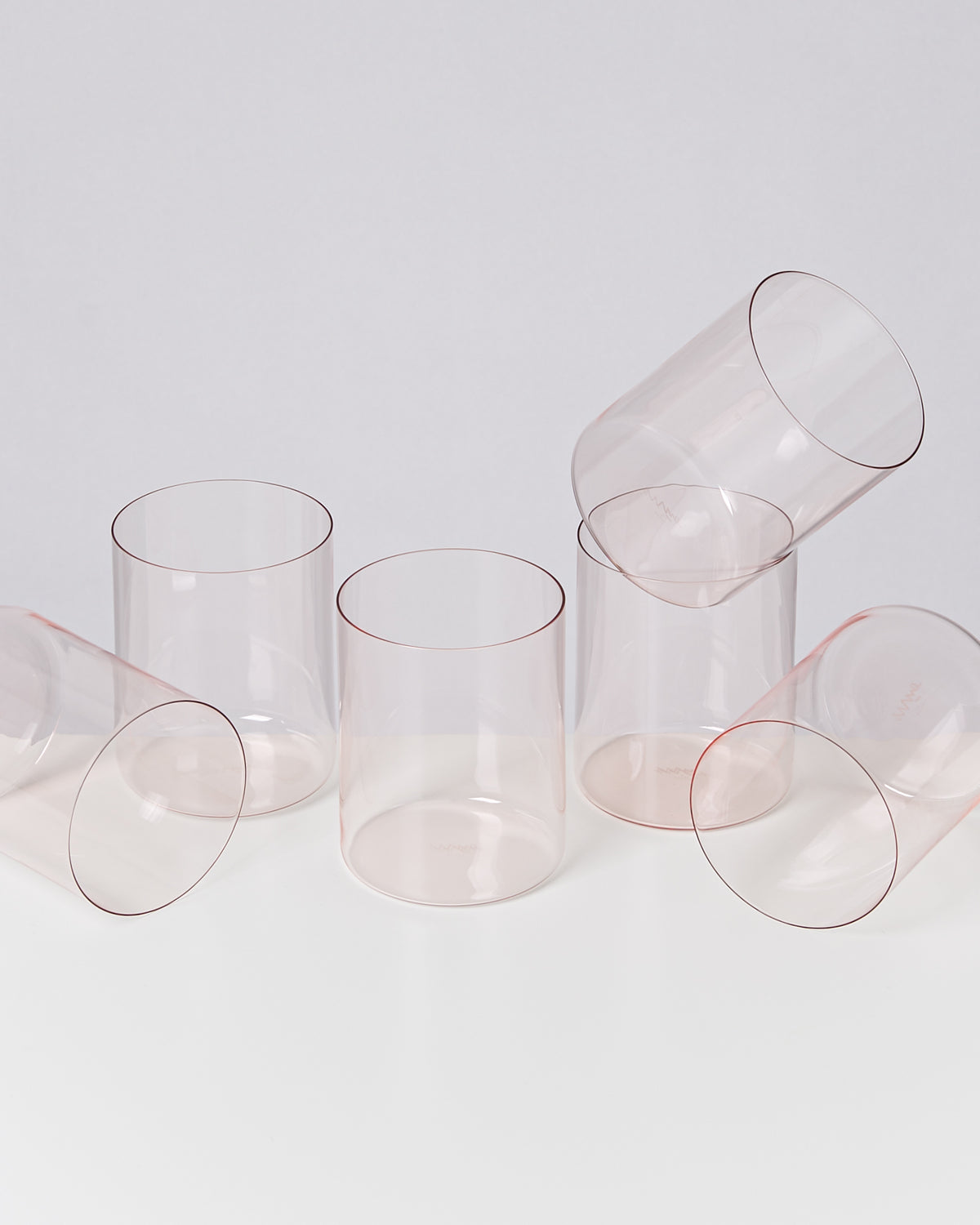 Sechs transparente Gläser, von denen einige aufrecht stehen und andere liegen auf einer weißen Oberfläche.