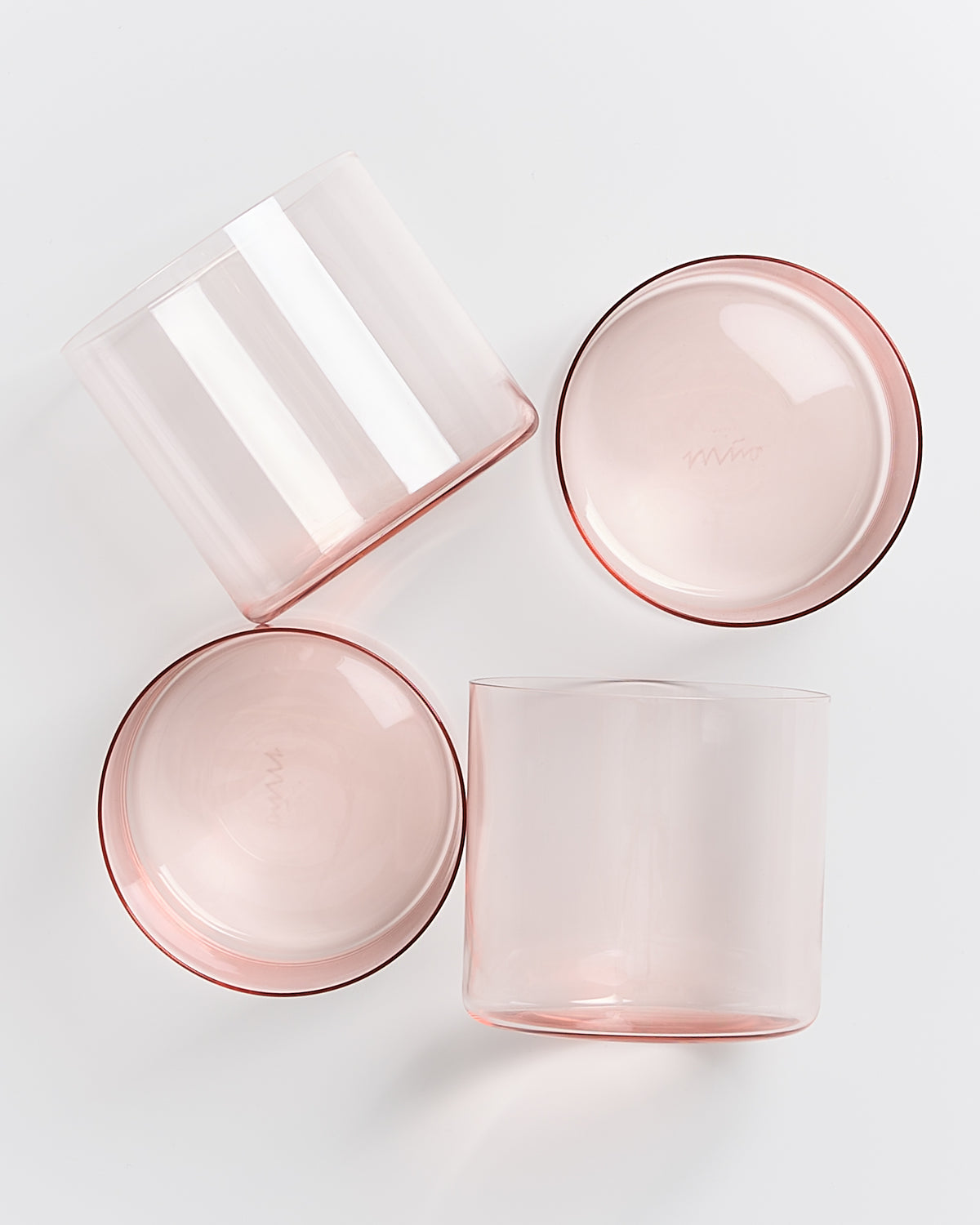 Vier rosa Gläser liegen und stehen auf einer weißen Oberfläche, zwei sichtbar von oben.
