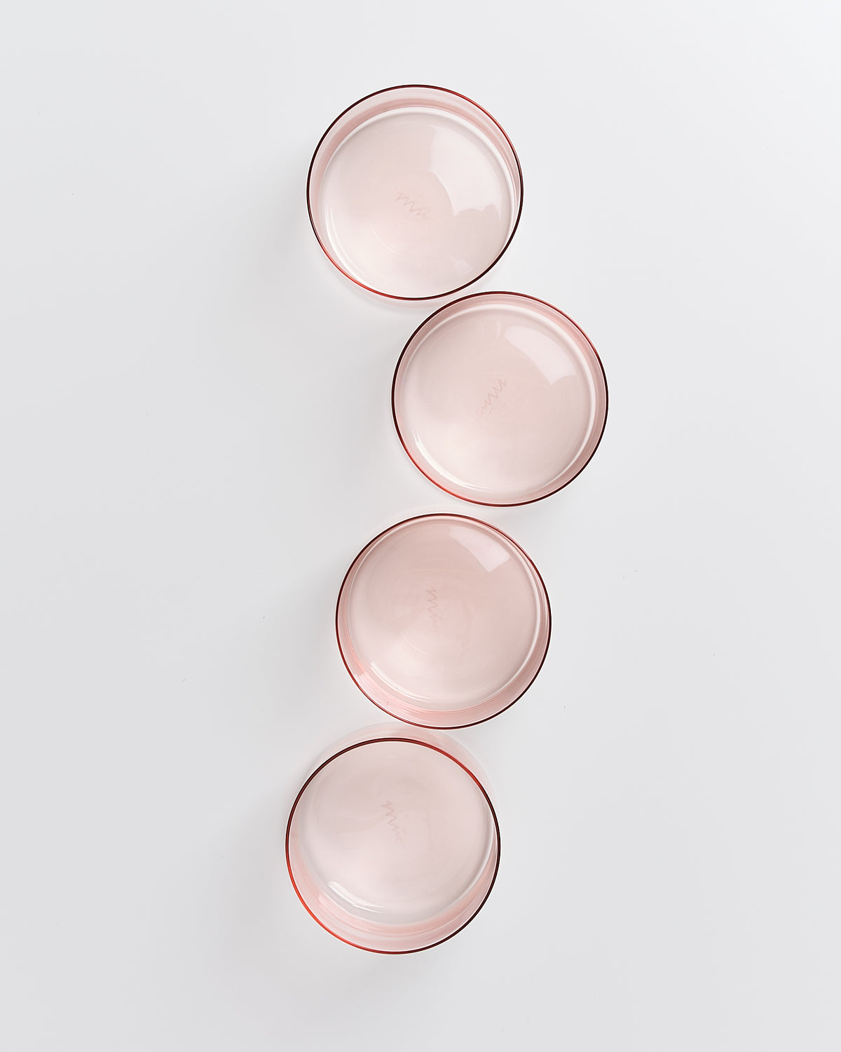 Vier runde, rosa Glasschalen sind in einer diagonalen Linie auf weißem Hintergrund angeordnet.