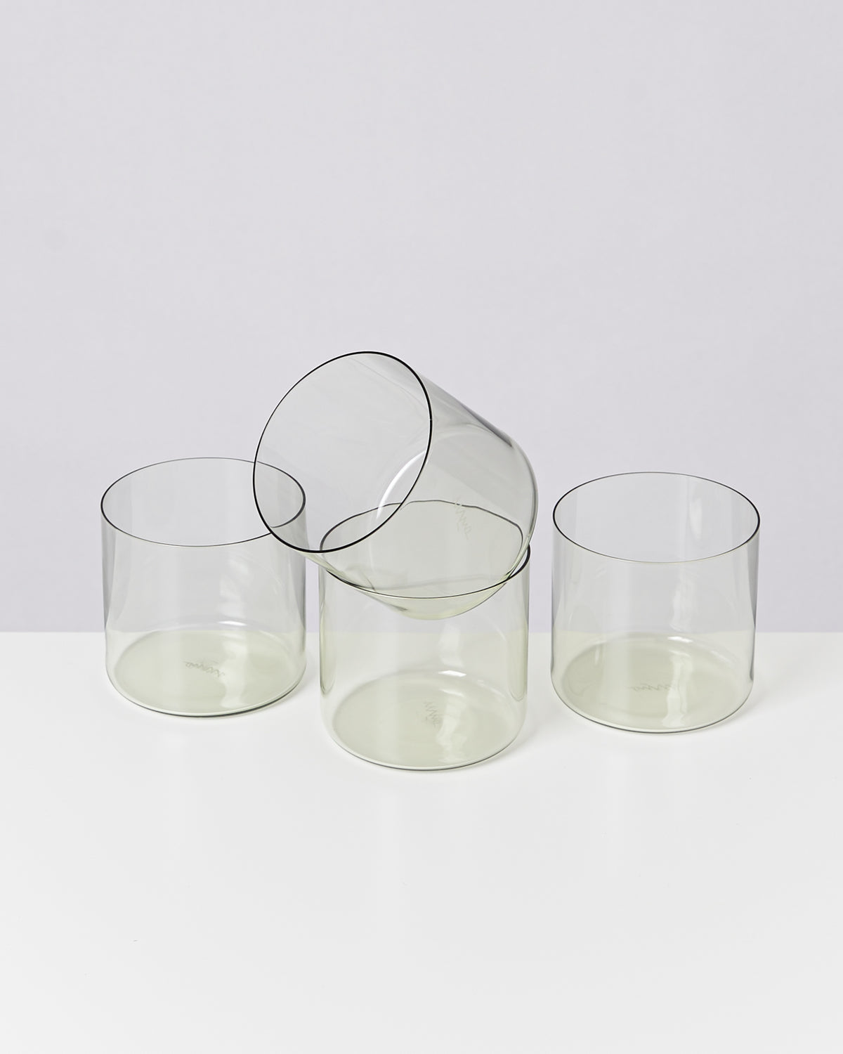 Vier durchsichtige Glasbecher auf einem weißen Hintergrund, einer liegt umgekippt auf den anderen.