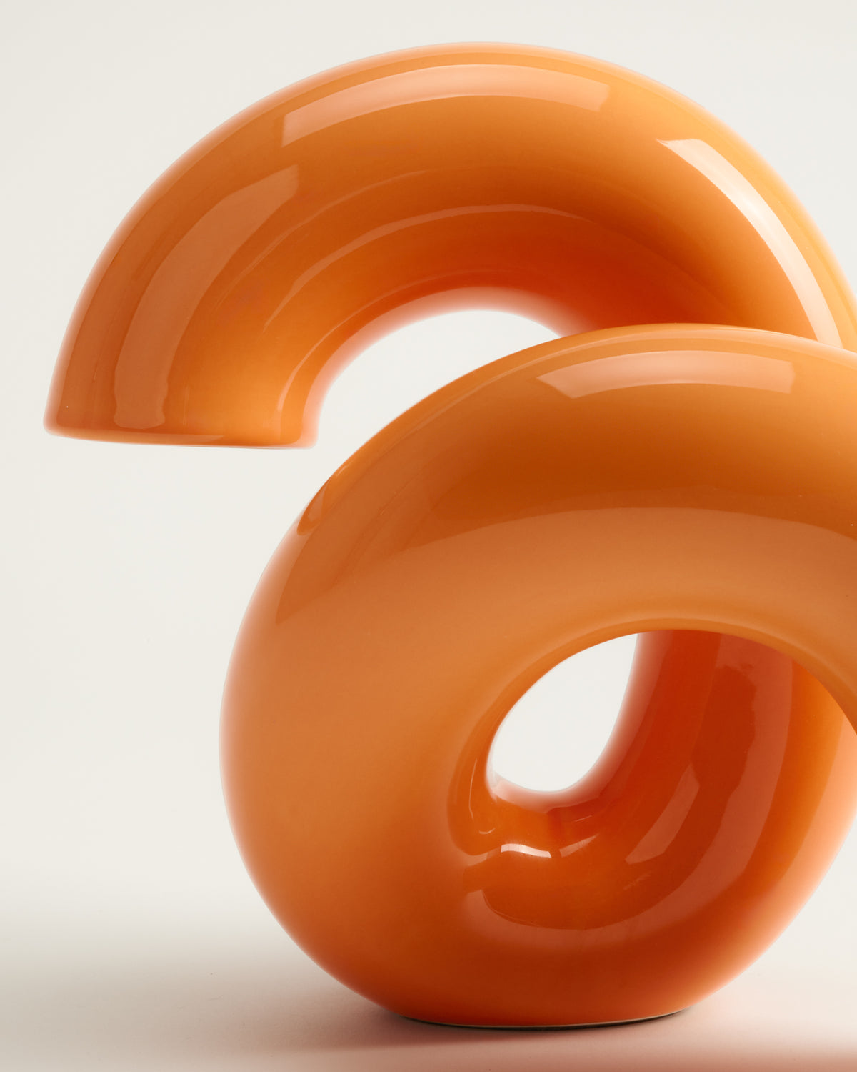 Orange, gebogene Skulptur mit glatter Oberfläche vor hellem Hintergrund.
