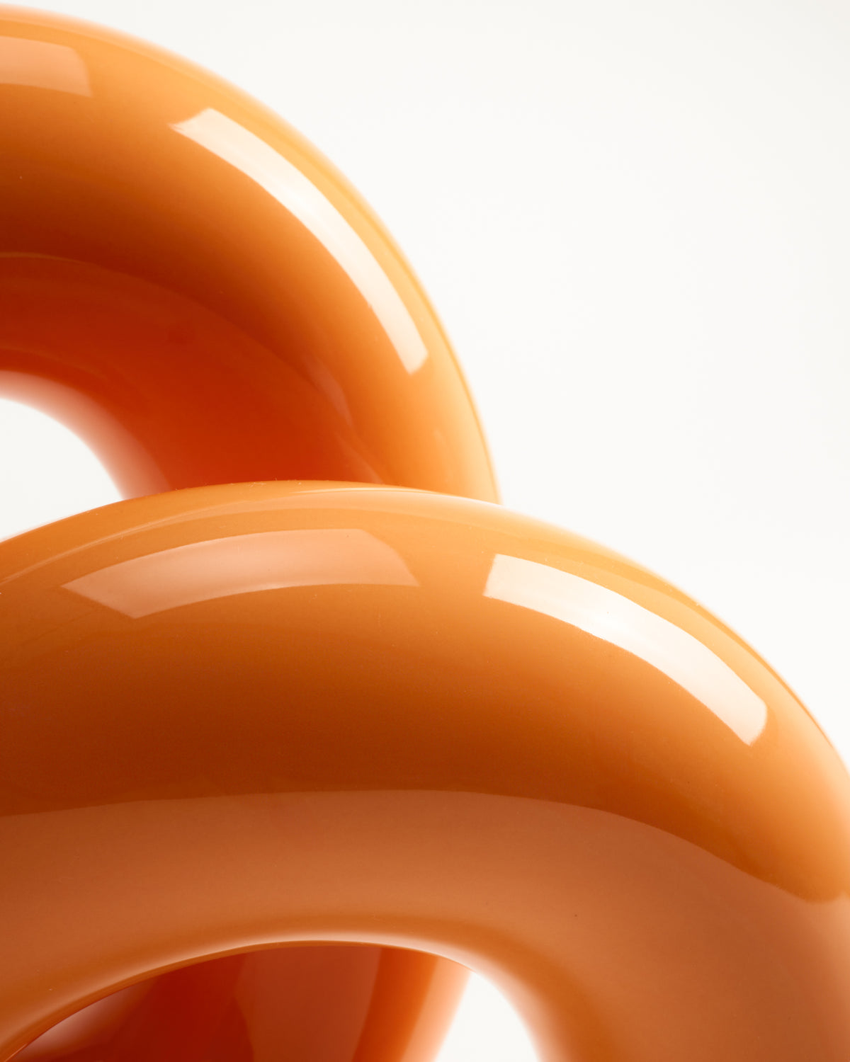 Zwei glänzende, orangefarbene, geschwungene Röhren vor einem hellen Hintergrund.