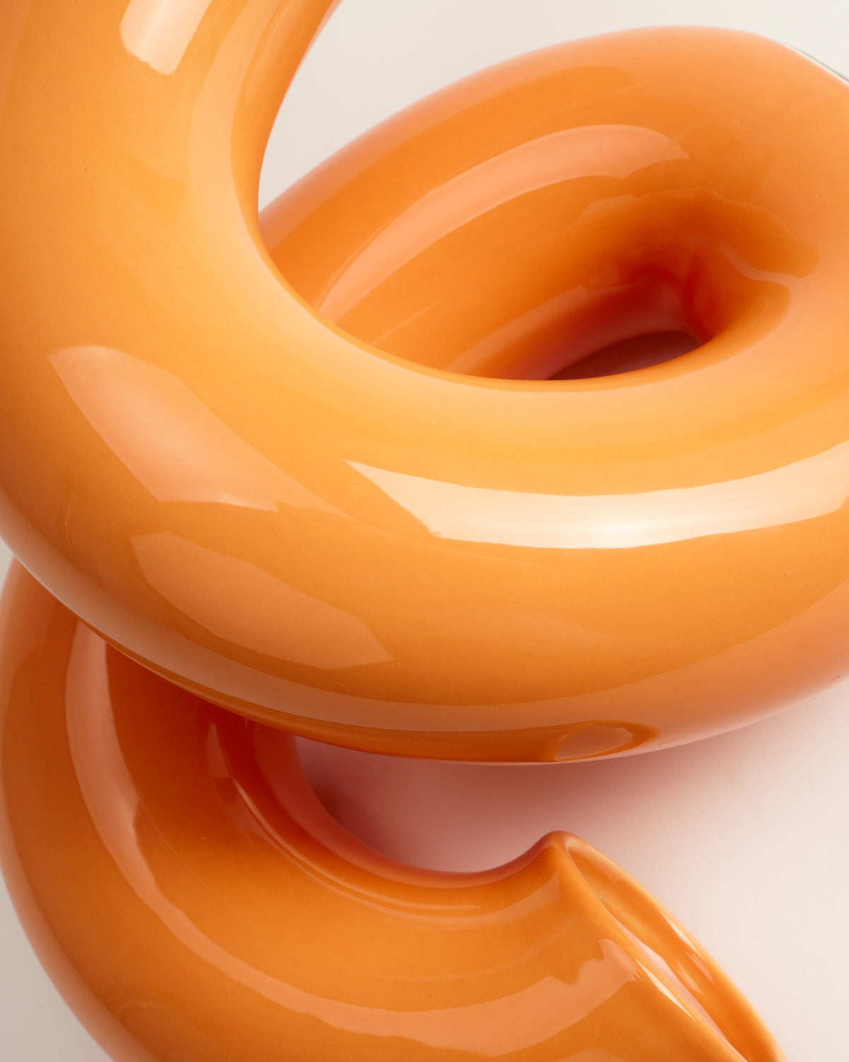 Orange, glänzende, ineinander verschlungene Skulptur mit sanften Kurven und Reflexionen.