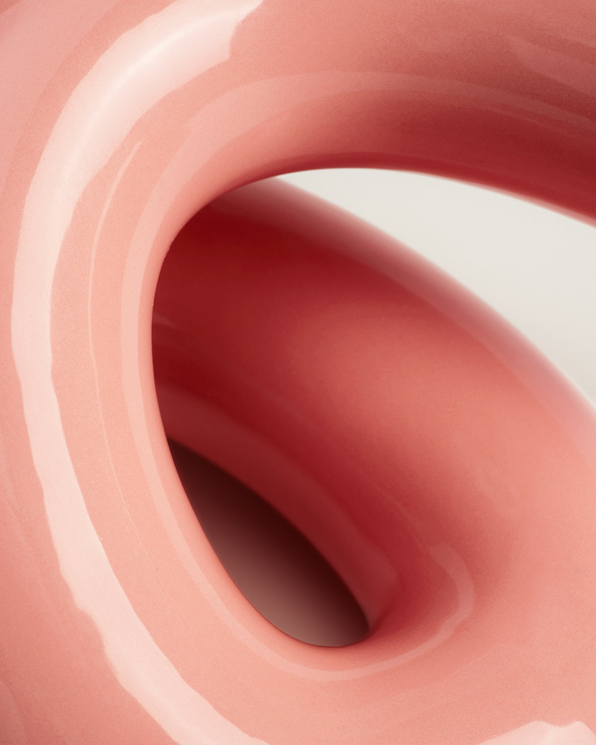 Nahaufnahme einer glänzenden, rosa-skulpturalen Form mit glatten Kurven und organischen Linien auf hellem Hintergrund.