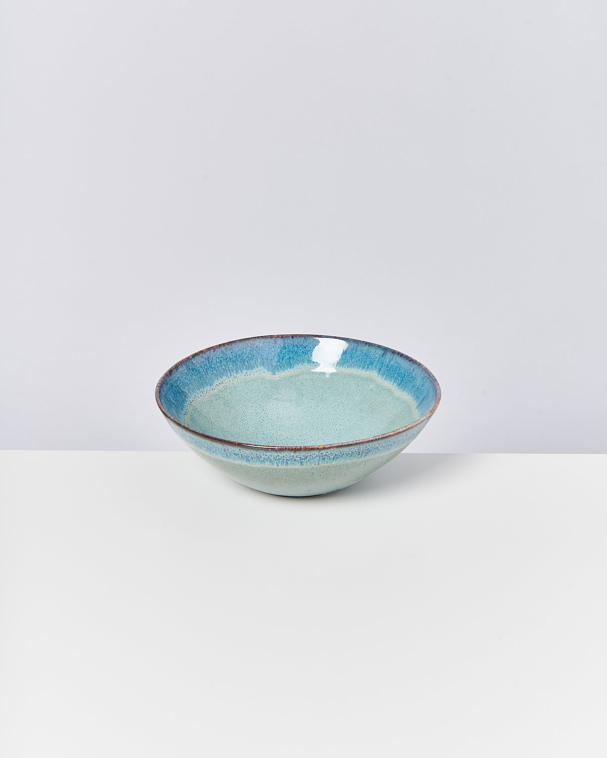 Keramikschale mit blau-grüner Glasur auf weißem Hintergrund.