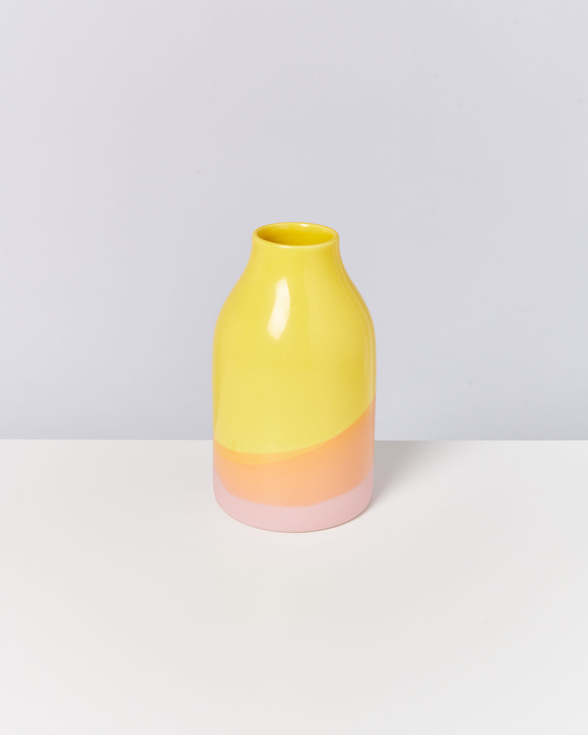 Gelbe Vase mit rosa und orangefarbenem Boden auf weißem Untergrund.