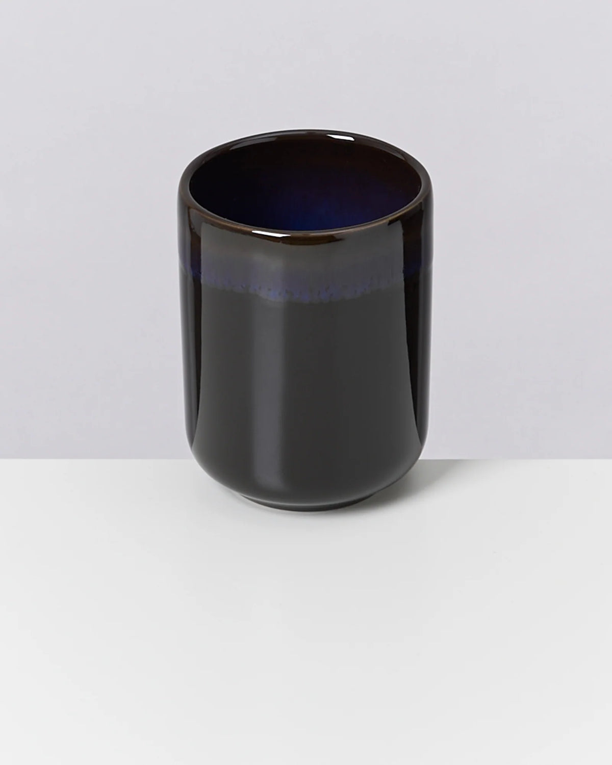 Dunkle, glänzende Tasse mit blauem Innenrand steht auf einem weißen Untergrund.