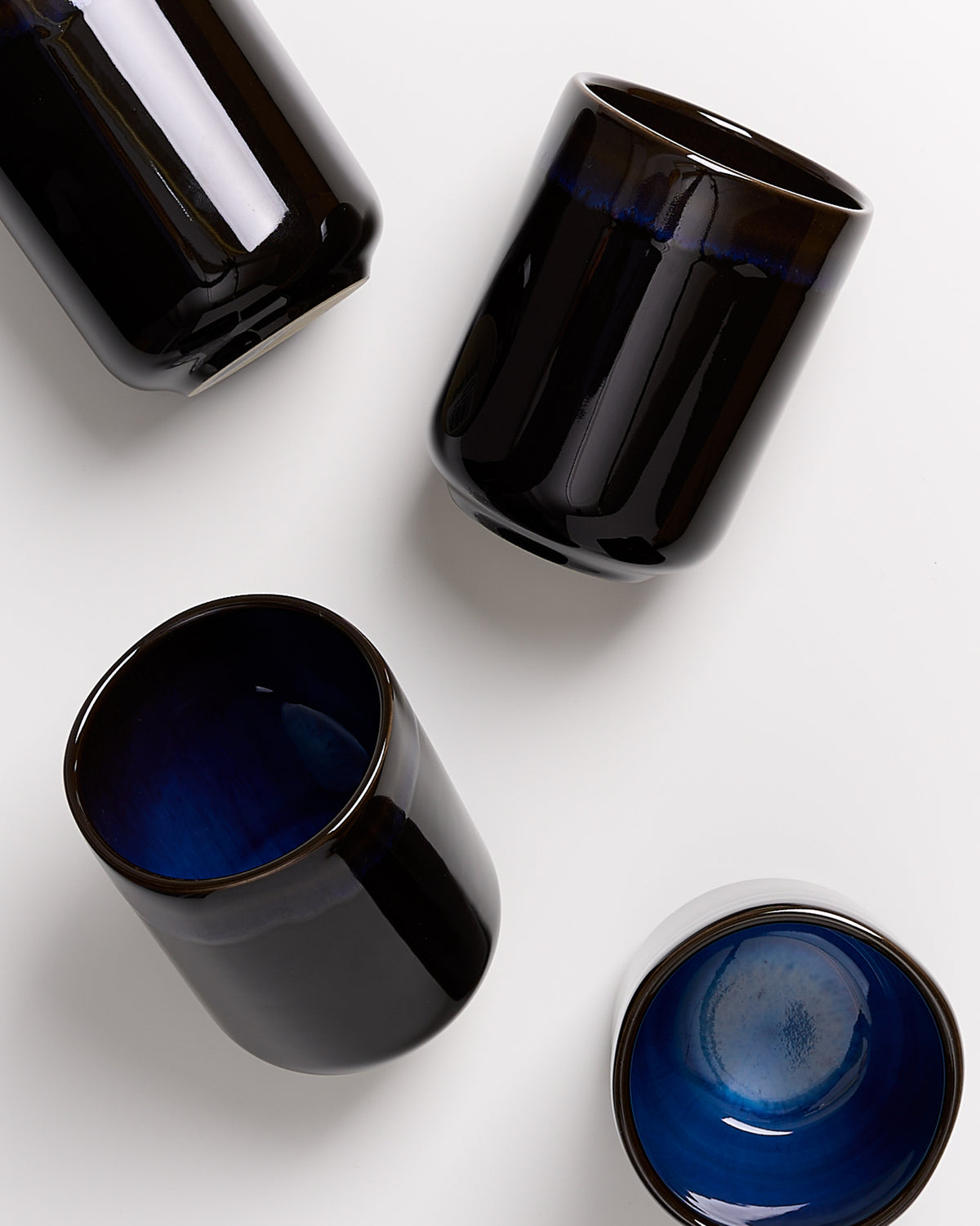 Vier schwarze Keramiktassen mit blauer Innenfläche auf weißem Hintergrund.